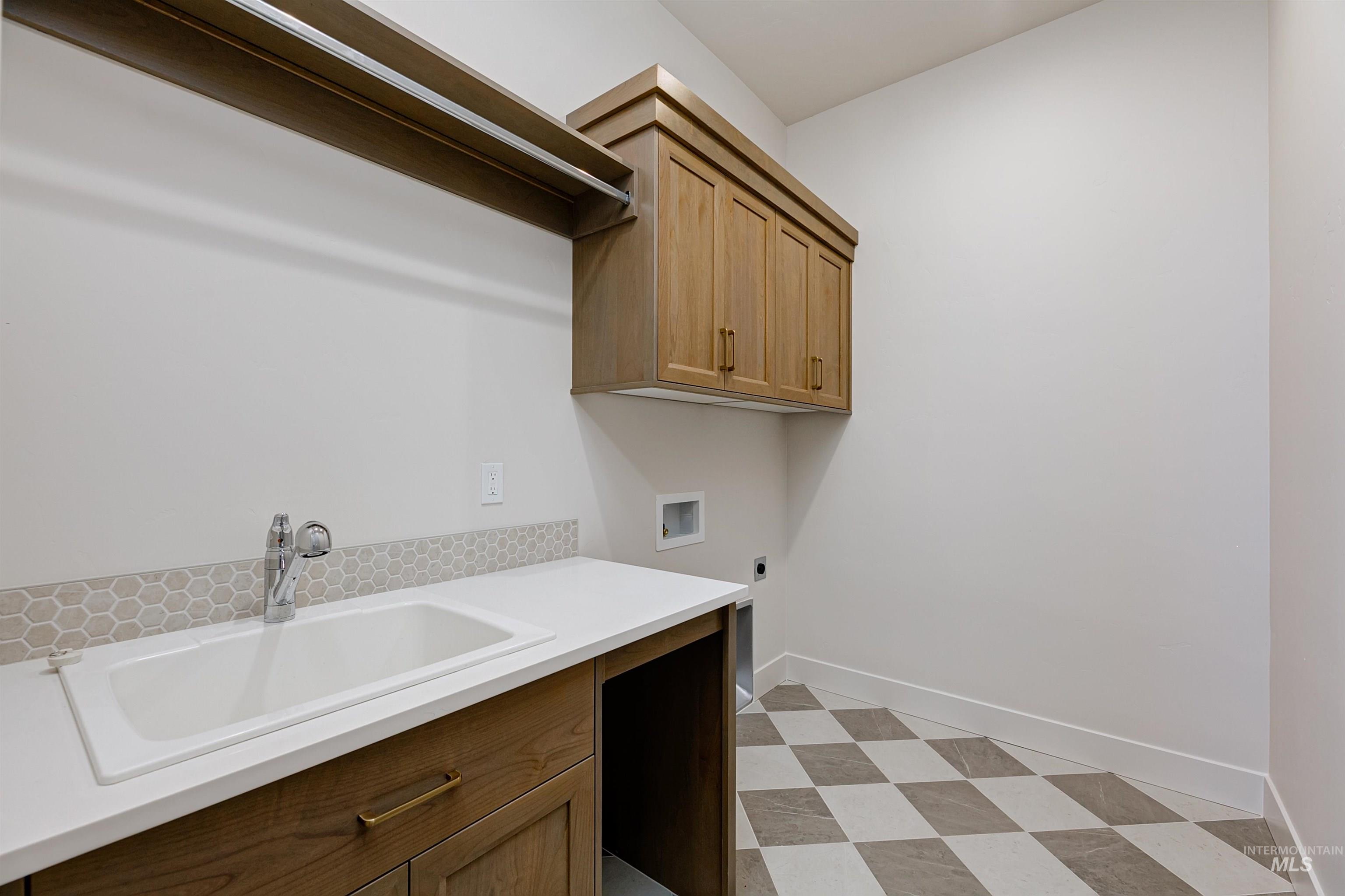 Laundry room featuring a deep utility sink, wood-finish cabinetry, white solid surface countertop, hexagonal tile backsplash, and checkerboard floor tiling