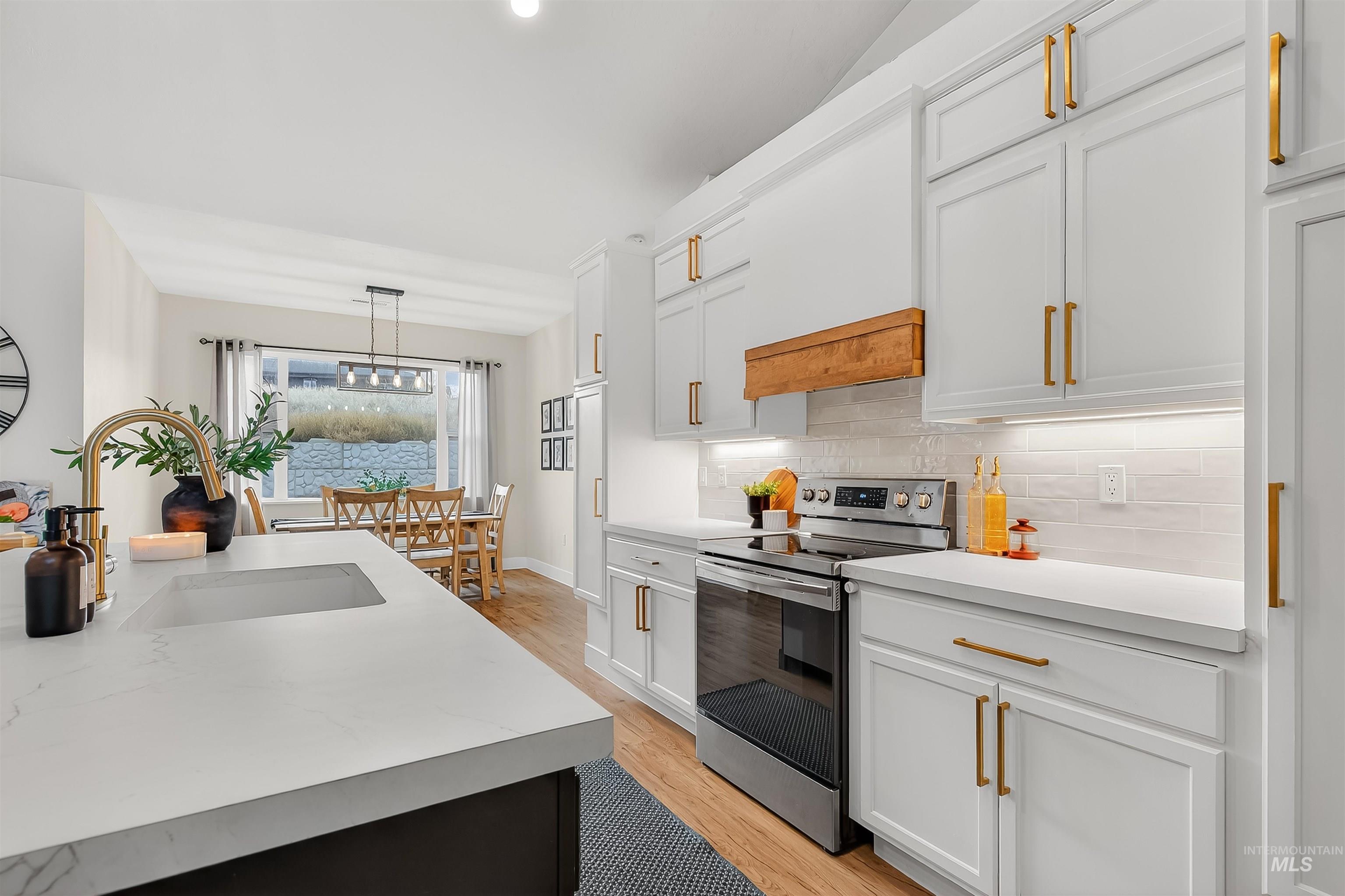 Kitchen with electric stove, light countertops, white cabinets, and hanging light fixtures