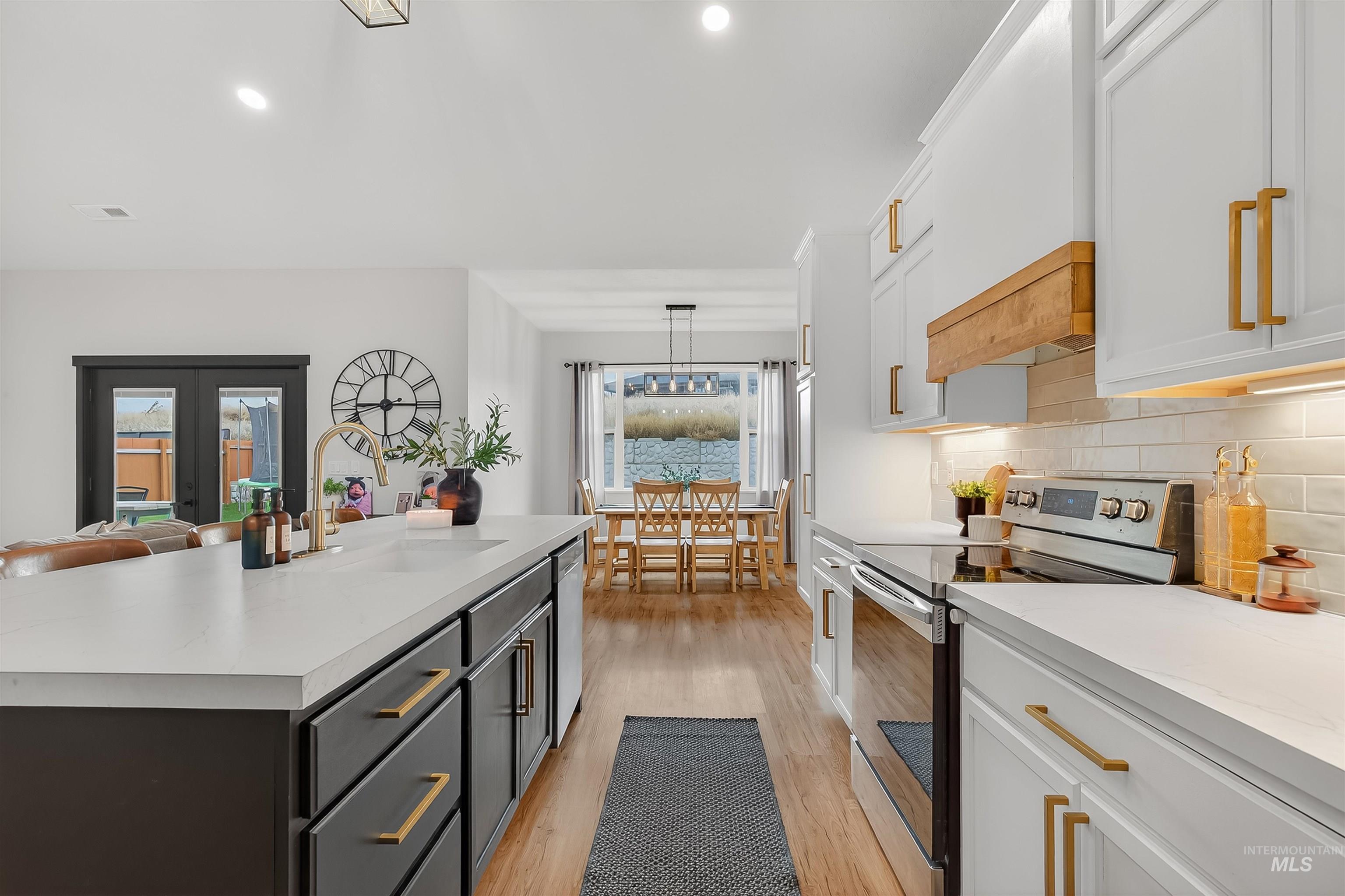 Kitchen with appliances with stainless steel finishes, white cabinets, backsplash, light wood-type flooring, and hanging light fixtures