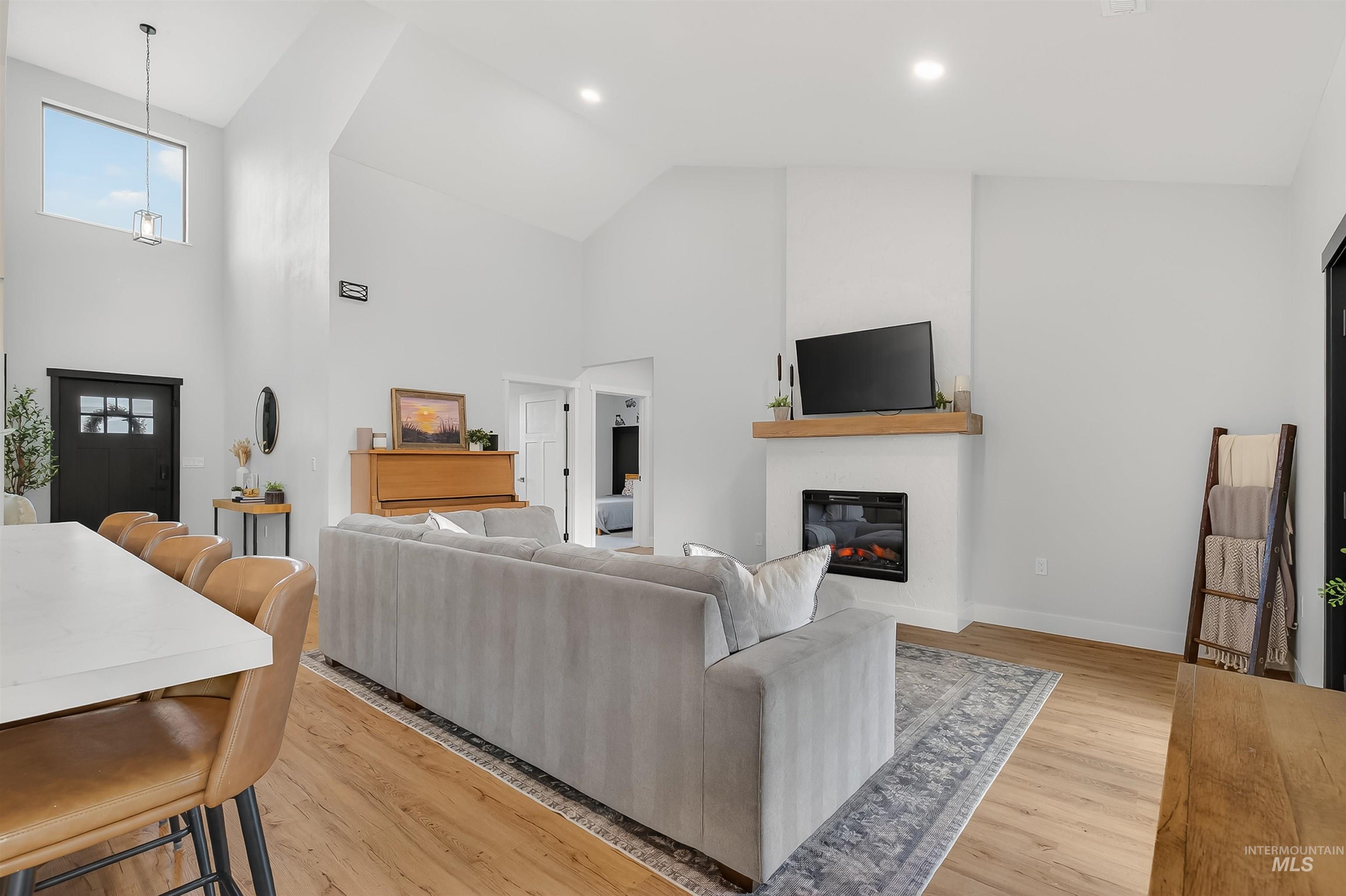 Living room featuring a glass covered fireplace, light wood-style flooring, and high vaulted ceiling