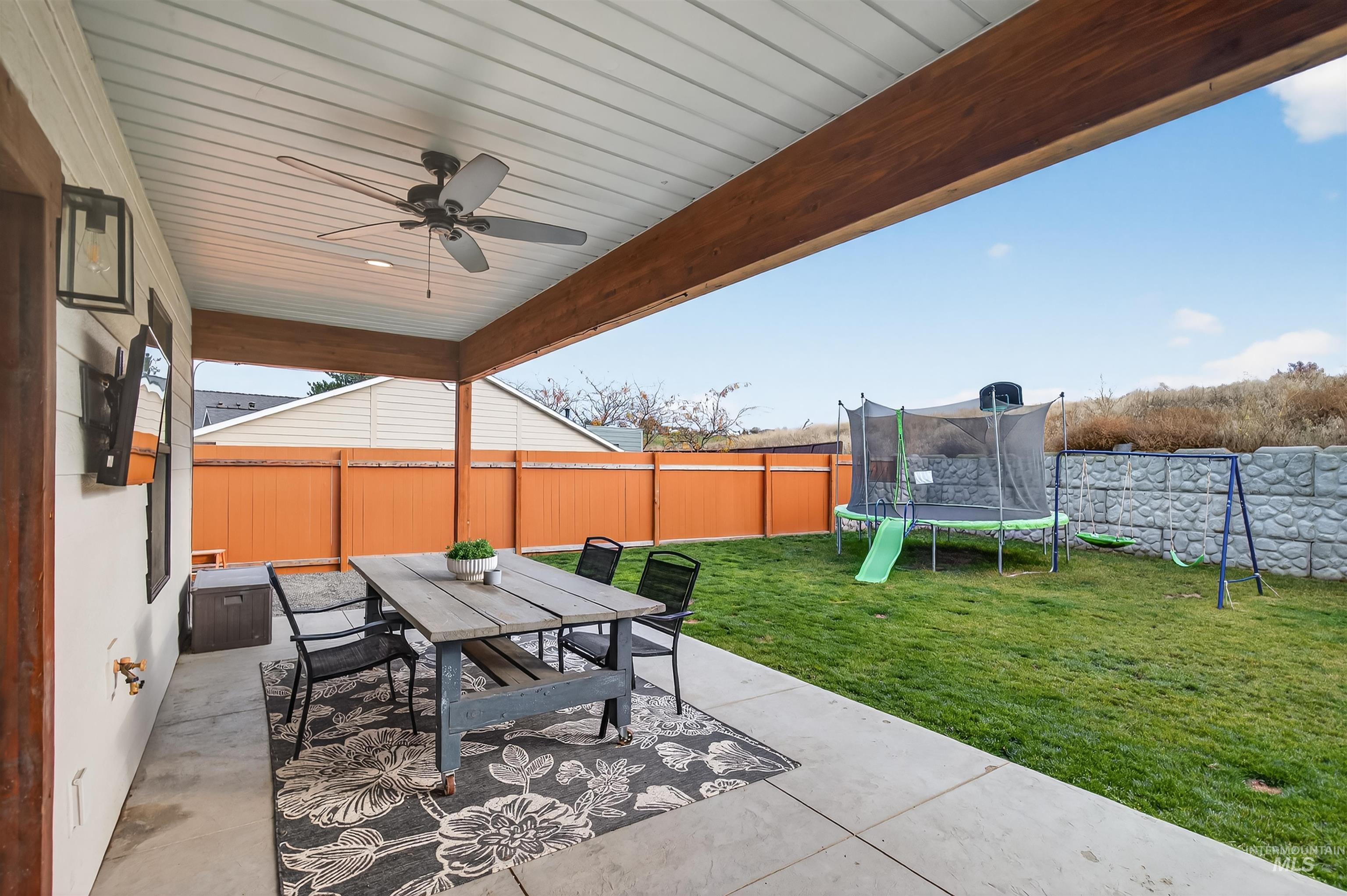 Fenced backyard featuring outdoor dining area, a patio, a trampoline, and ceiling fan