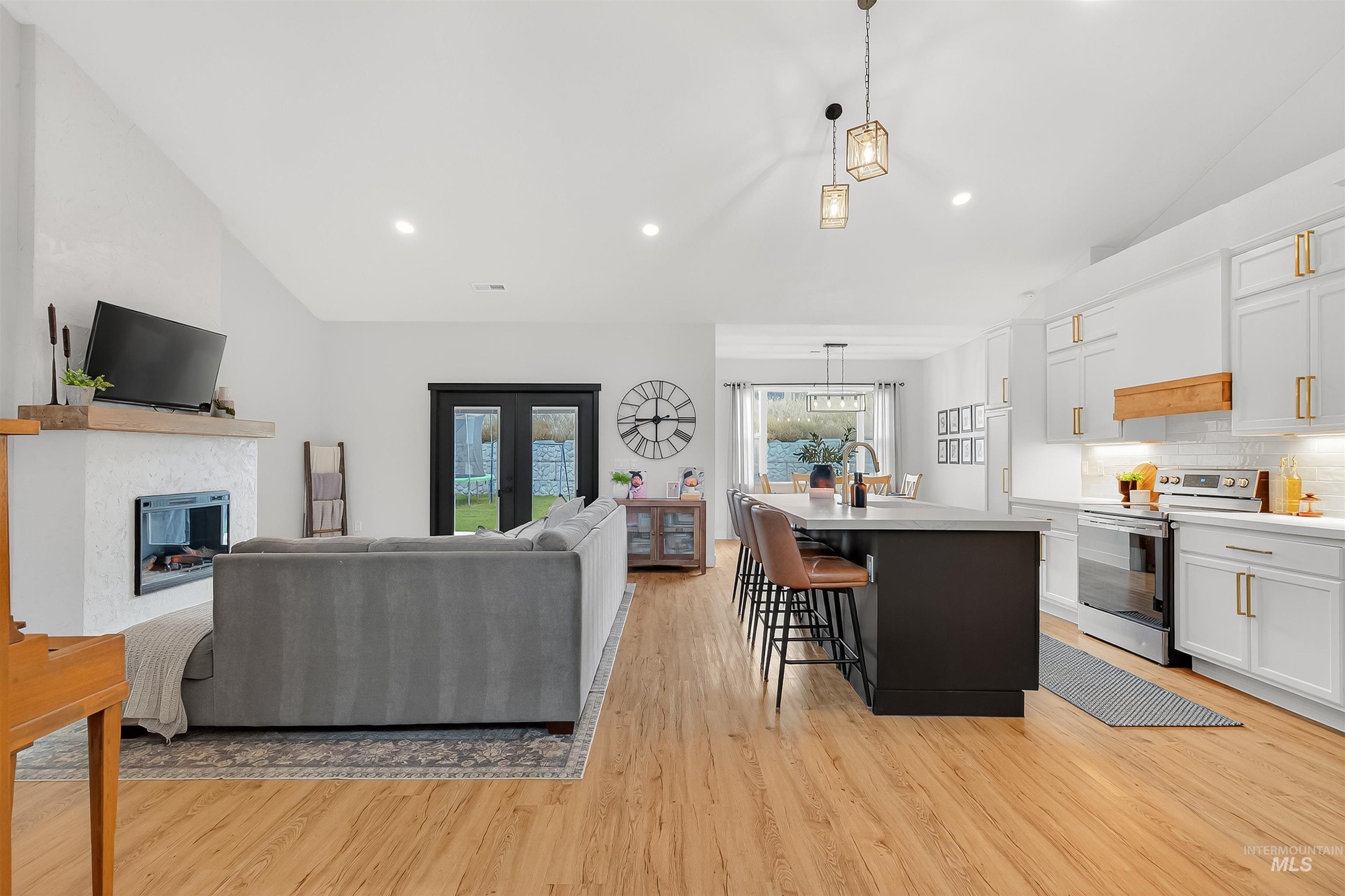 Living area with lofted ceiling, a glass covered fireplace, light wood-style flooring, recessed lighting, and french doors