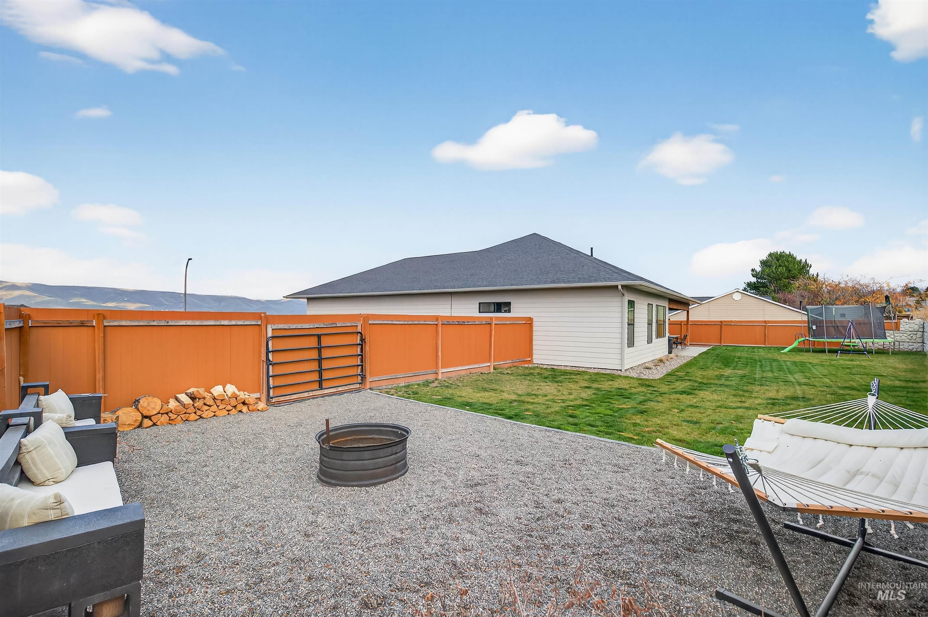 Fenced backyard with a trampoline, a fire pit, and a patio area