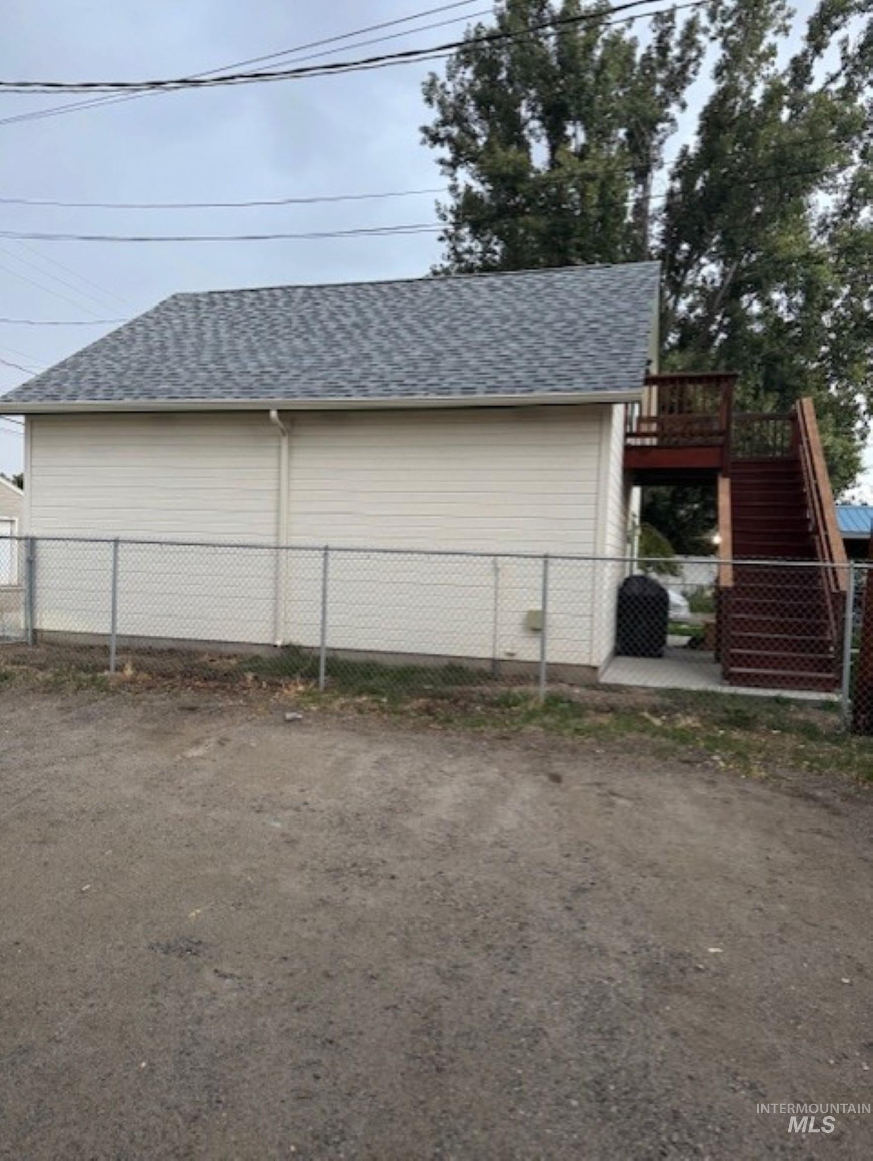 View of side of property featuring stairs, a shingled roof, and a patio area