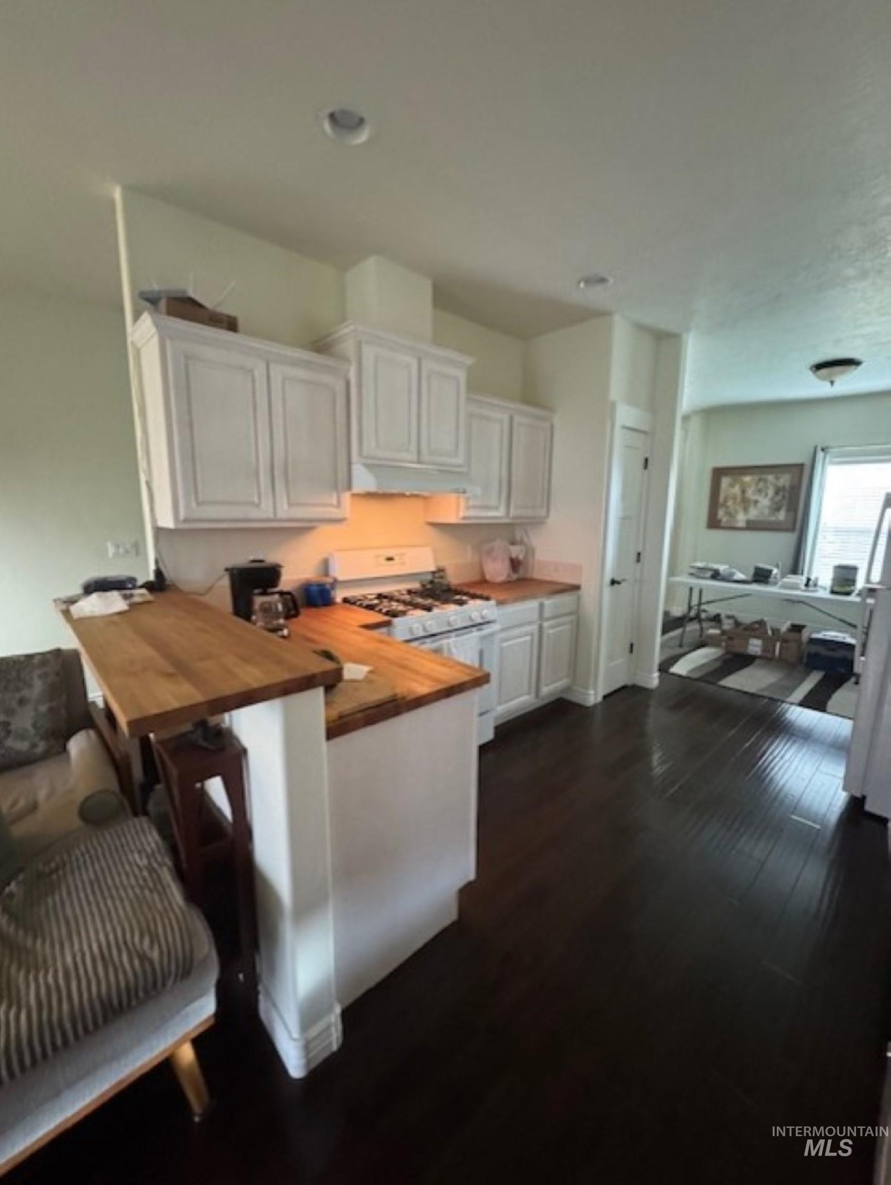 Kitchen with white cabinetry, gas range gas stove, wooden counters, dark wood-style flooring, and a peninsula