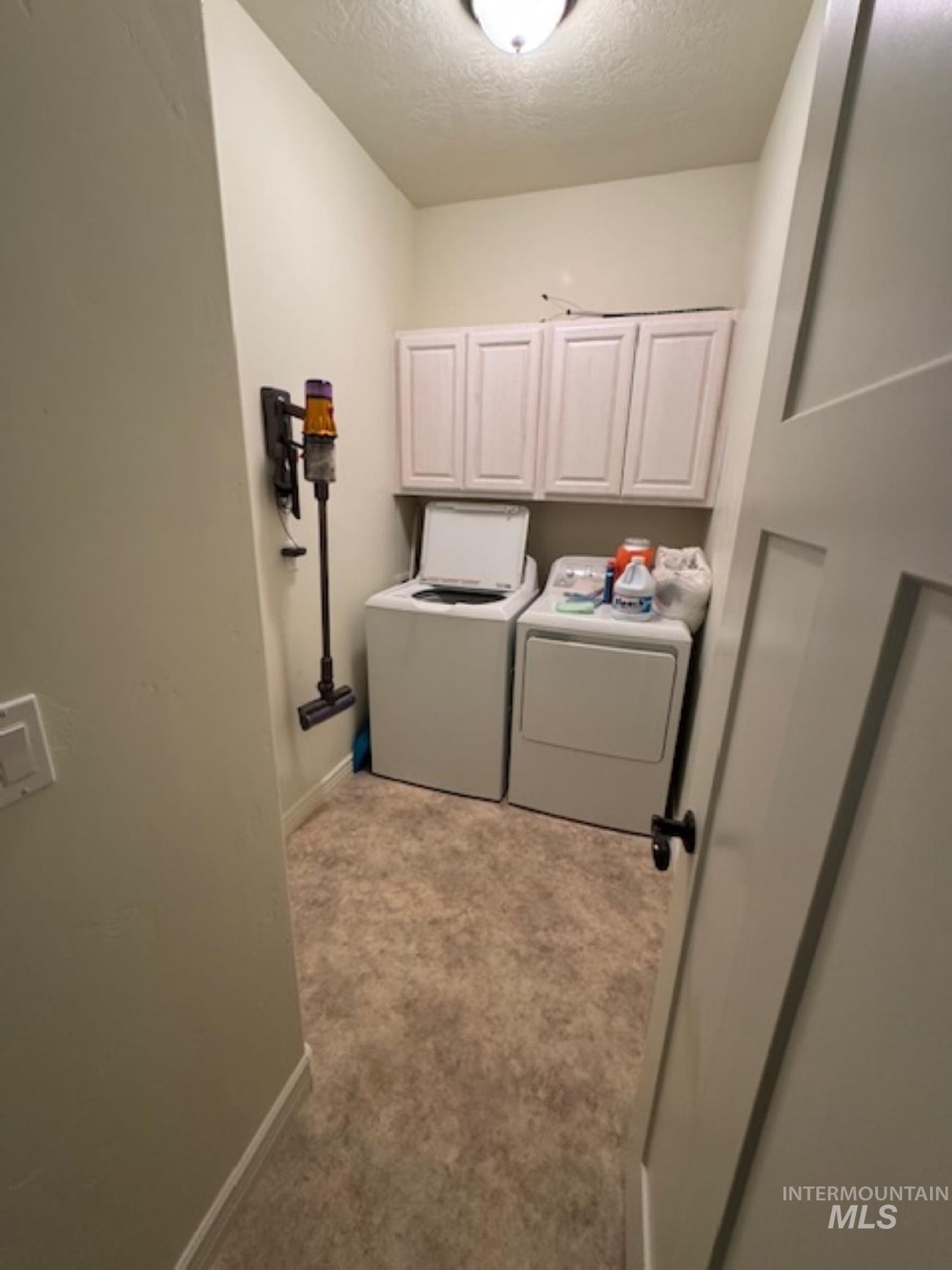 Laundry area with a textured ceiling, cabinet space, light colored carpet, and washer and clothes dryer