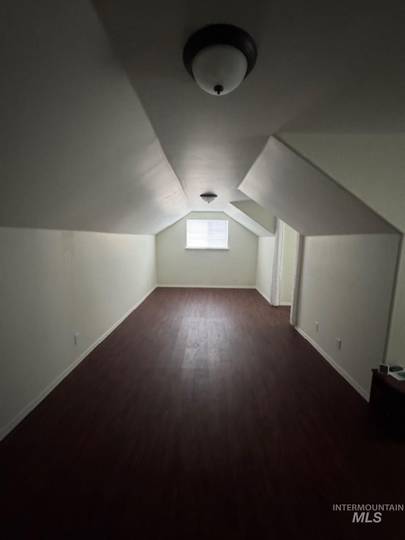 Bonus room with dark wood finished floors and vaulted ceiling