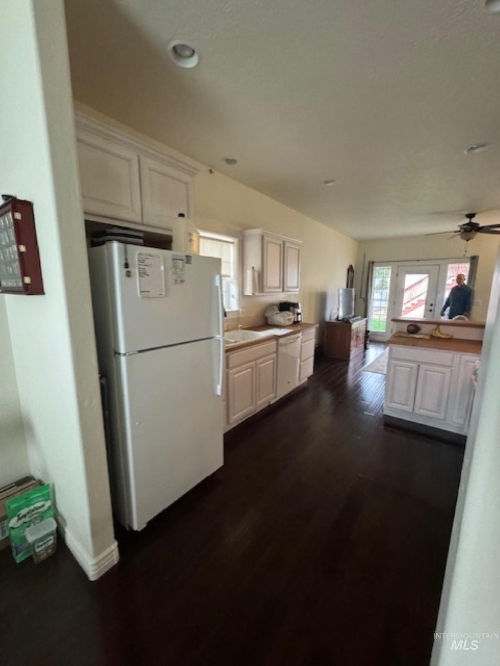 Kitchen with white appliances, dark wood-style floors, ceiling fan, light countertops, and white cabinets