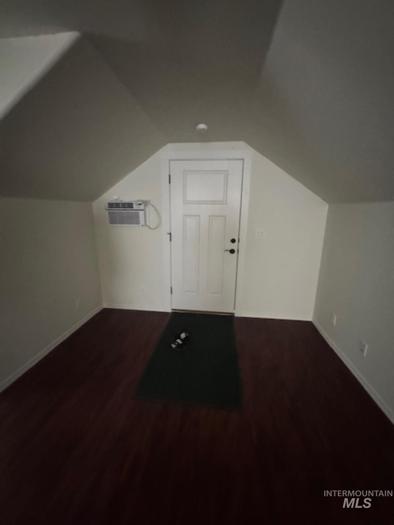 Additional living space featuring dark wood-style flooring, vaulted ceiling, and a wall mounted air conditioner