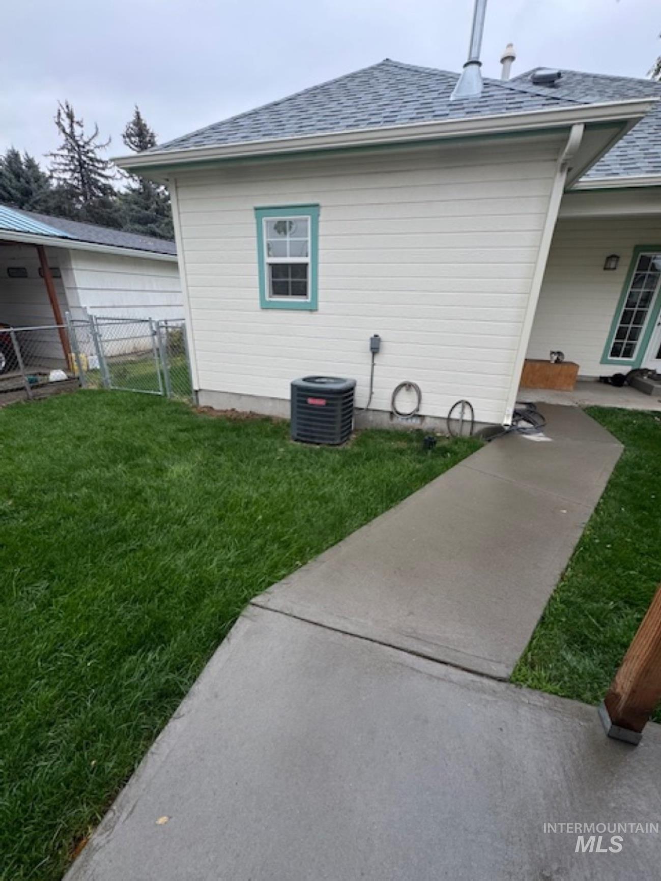 View of side of property with a shingled roof and a gate