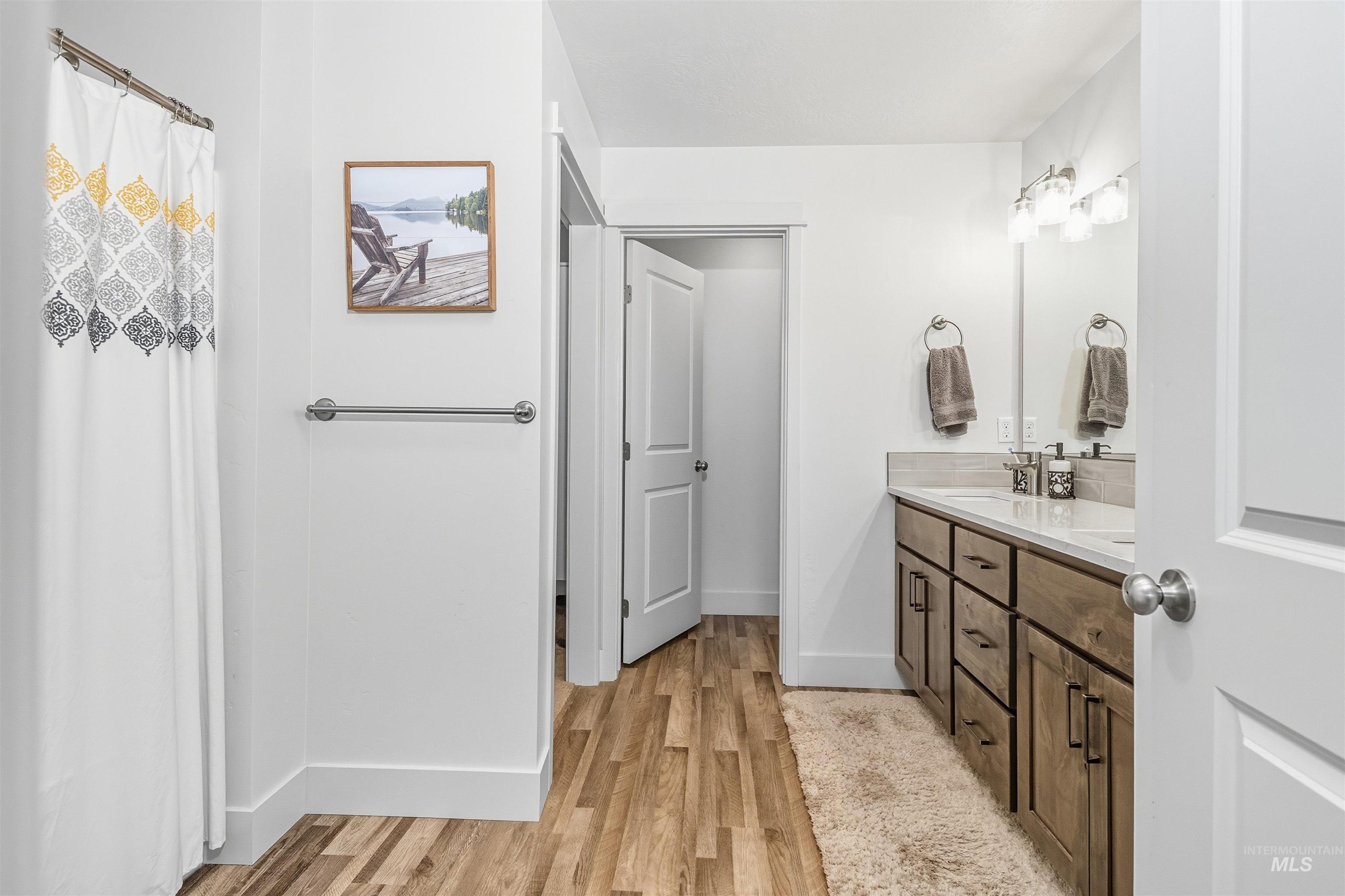 Full bath with double vanity, light wood-type flooring, and curtained shower
