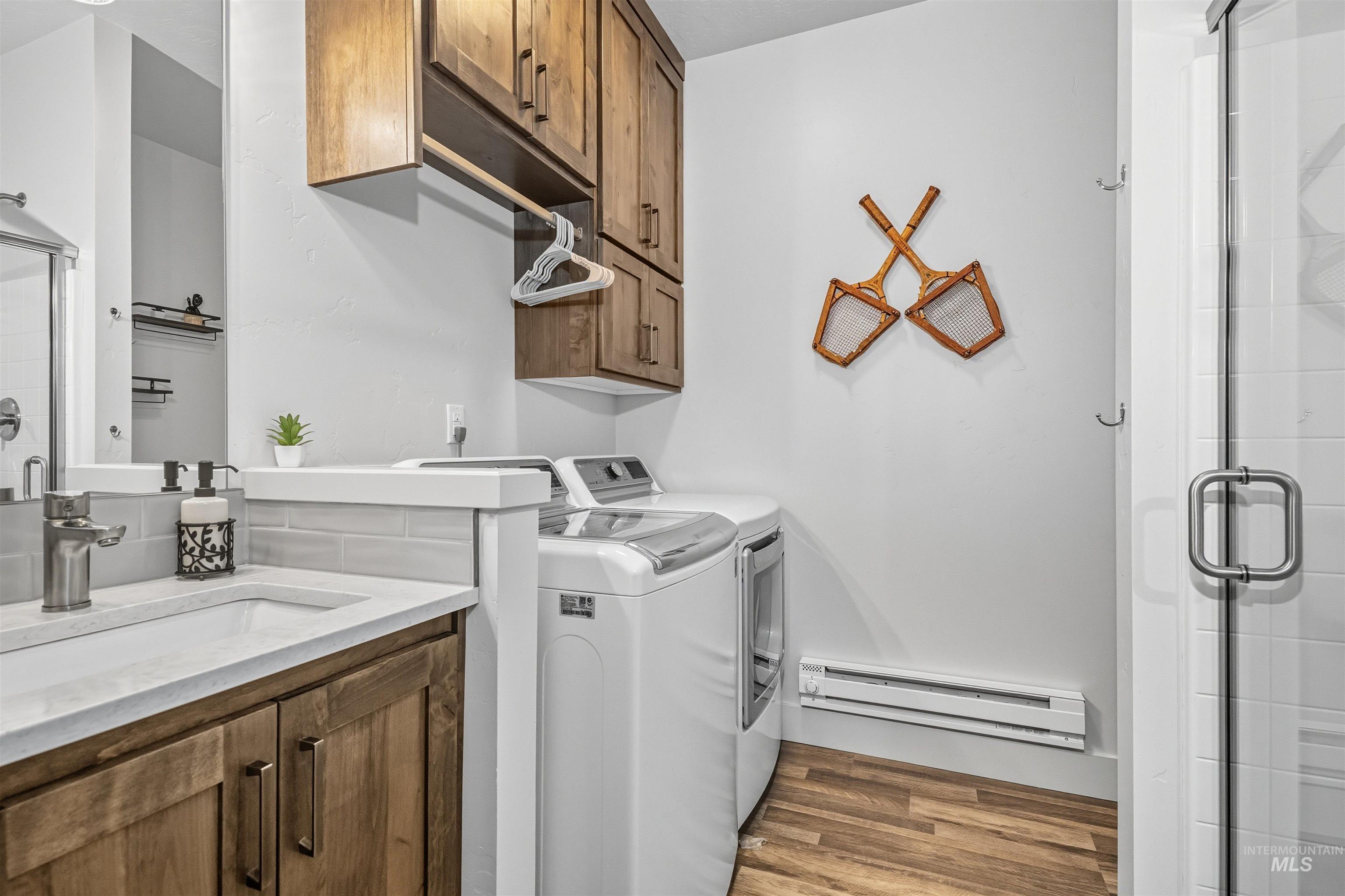 Laundry room with a baseboard heating unit, light wood-style floors, washing machine and clothes dryer, and cabinet space