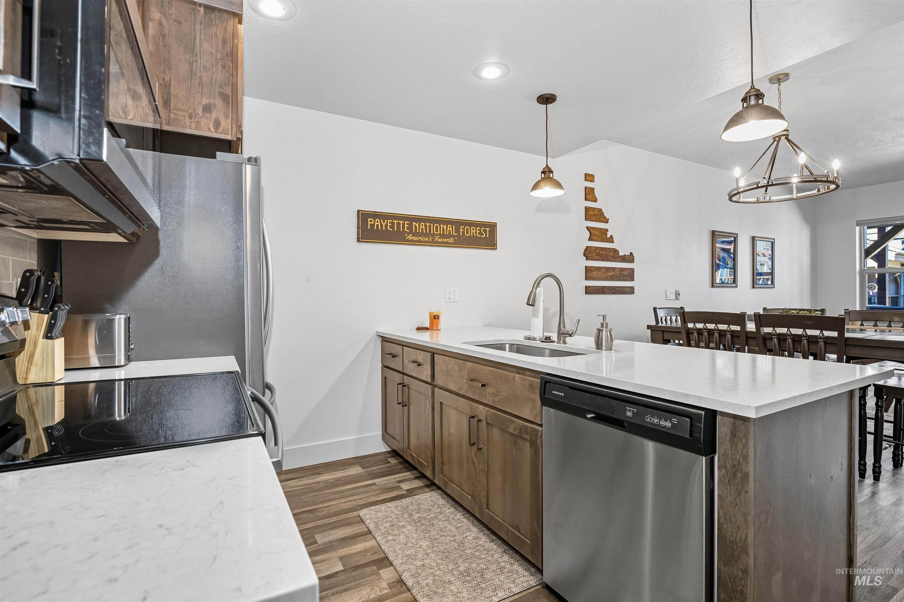 Kitchen with a peninsula, stainless steel appliances, pendant lighting, dark wood-type flooring, and a chandelier