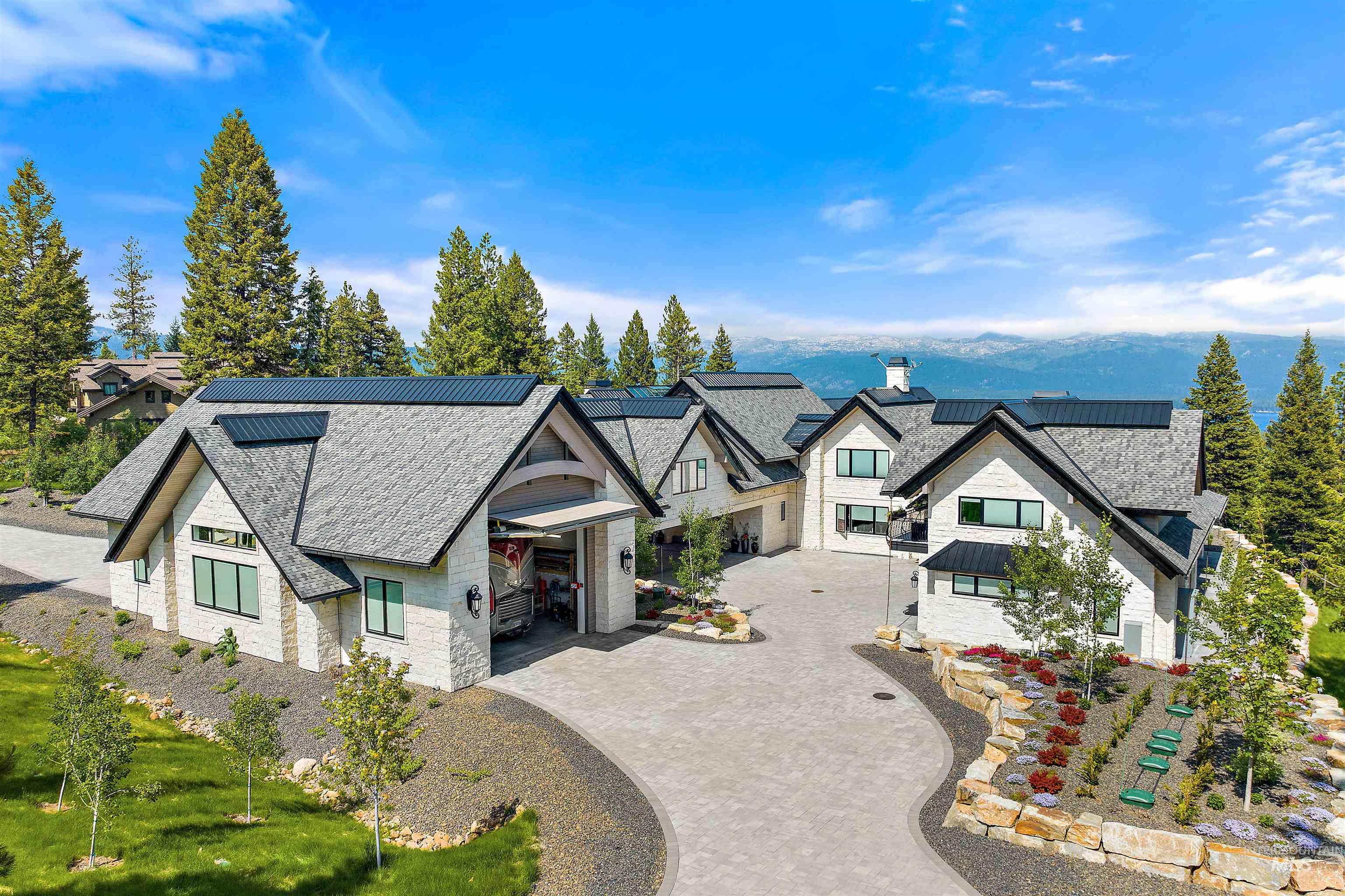 Expansive property featuring a multi-gabled residence with light-colored stone and siding, dark-toned roofing, and a substantial paved driveway