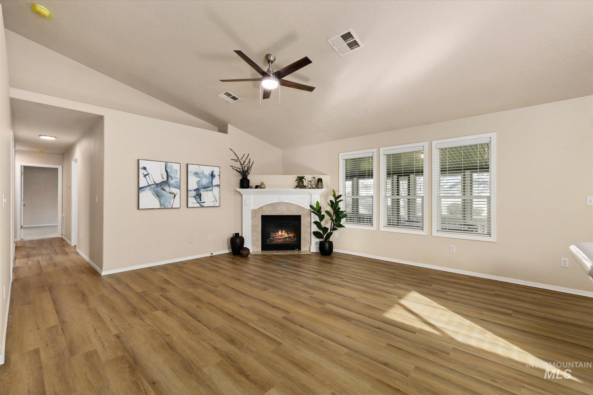 Unfurnished living room with a fireplace, vaulted ceiling, ceiling fan, and light wood-type flooring