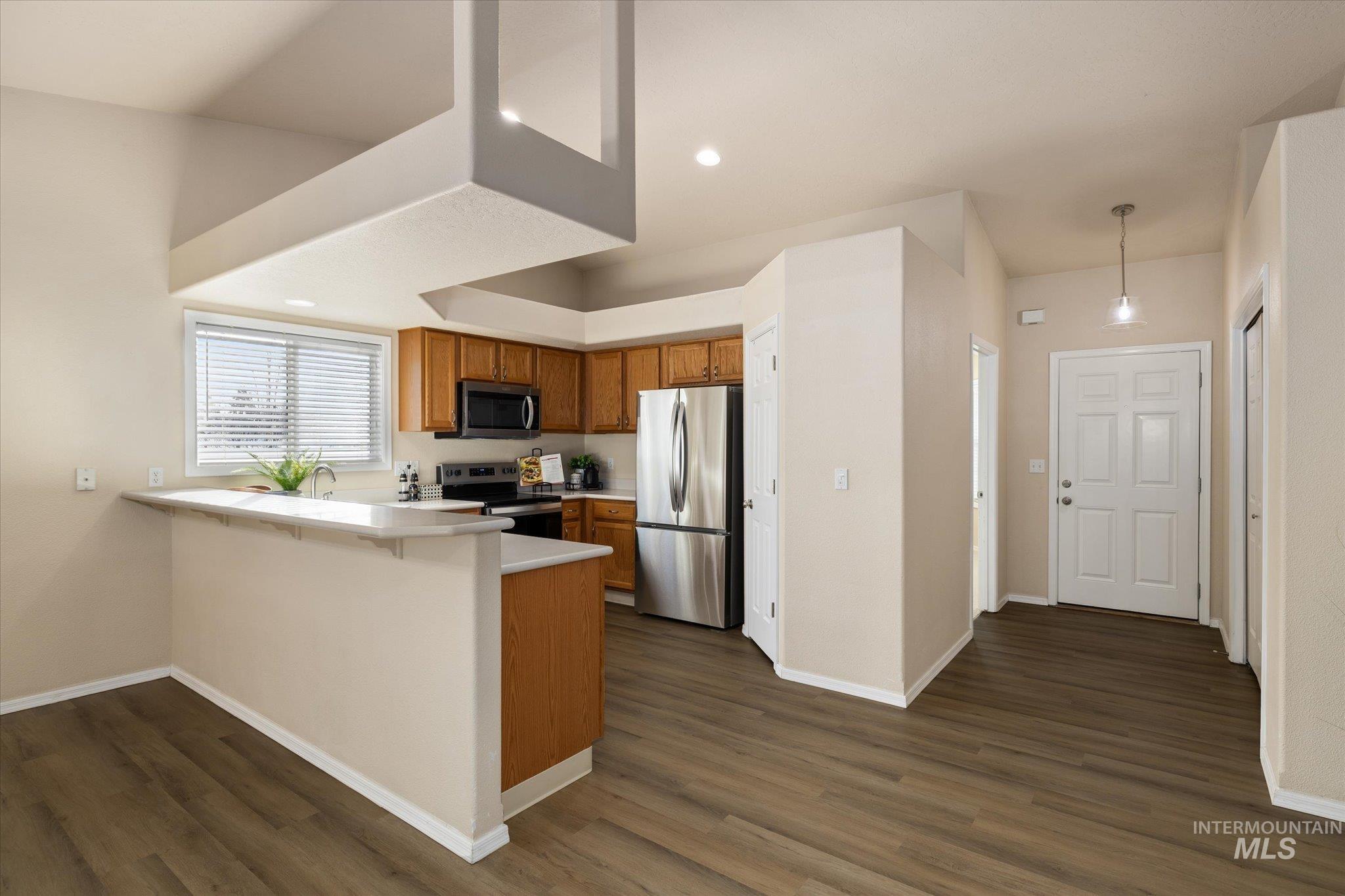 Kitchen with light countertops, brown cabinetry, a peninsula, appliances with stainless steel finishes, and decorative light fixtures