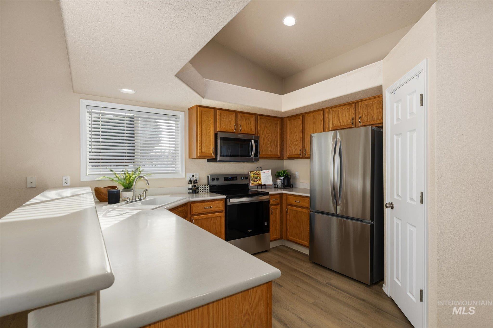 Kitchen featuring light countertops, stainless steel appliances, brown cabinetry, light wood-type flooring, and recessed lighting