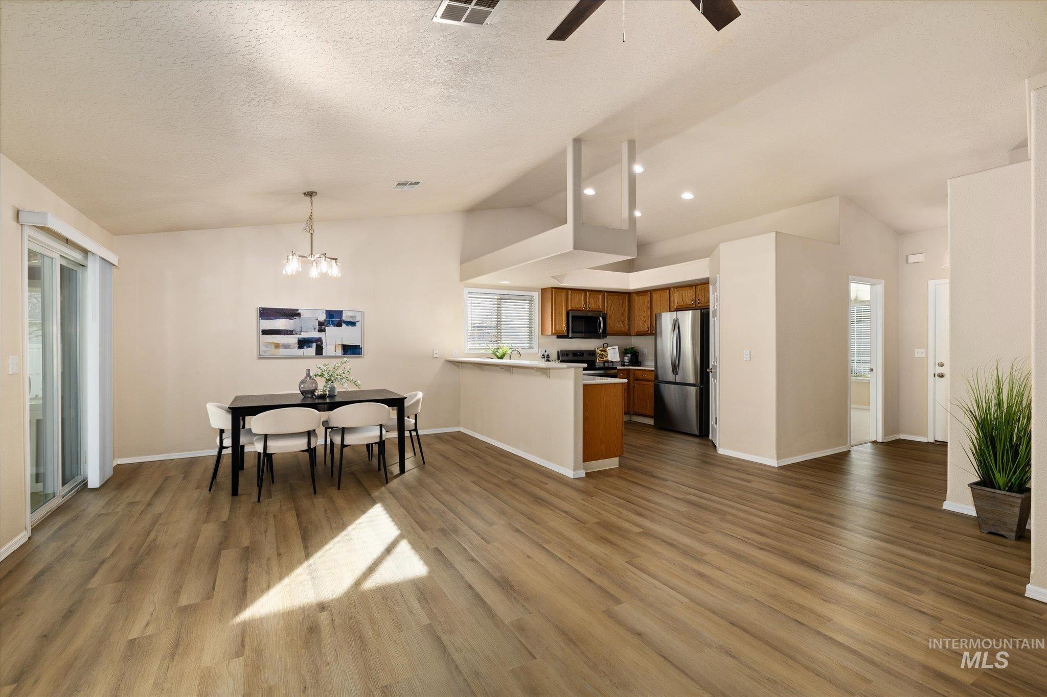 Kitchen featuring brown cabinetry, lofted ceiling, a peninsula, open floor plan, and pendant lighting