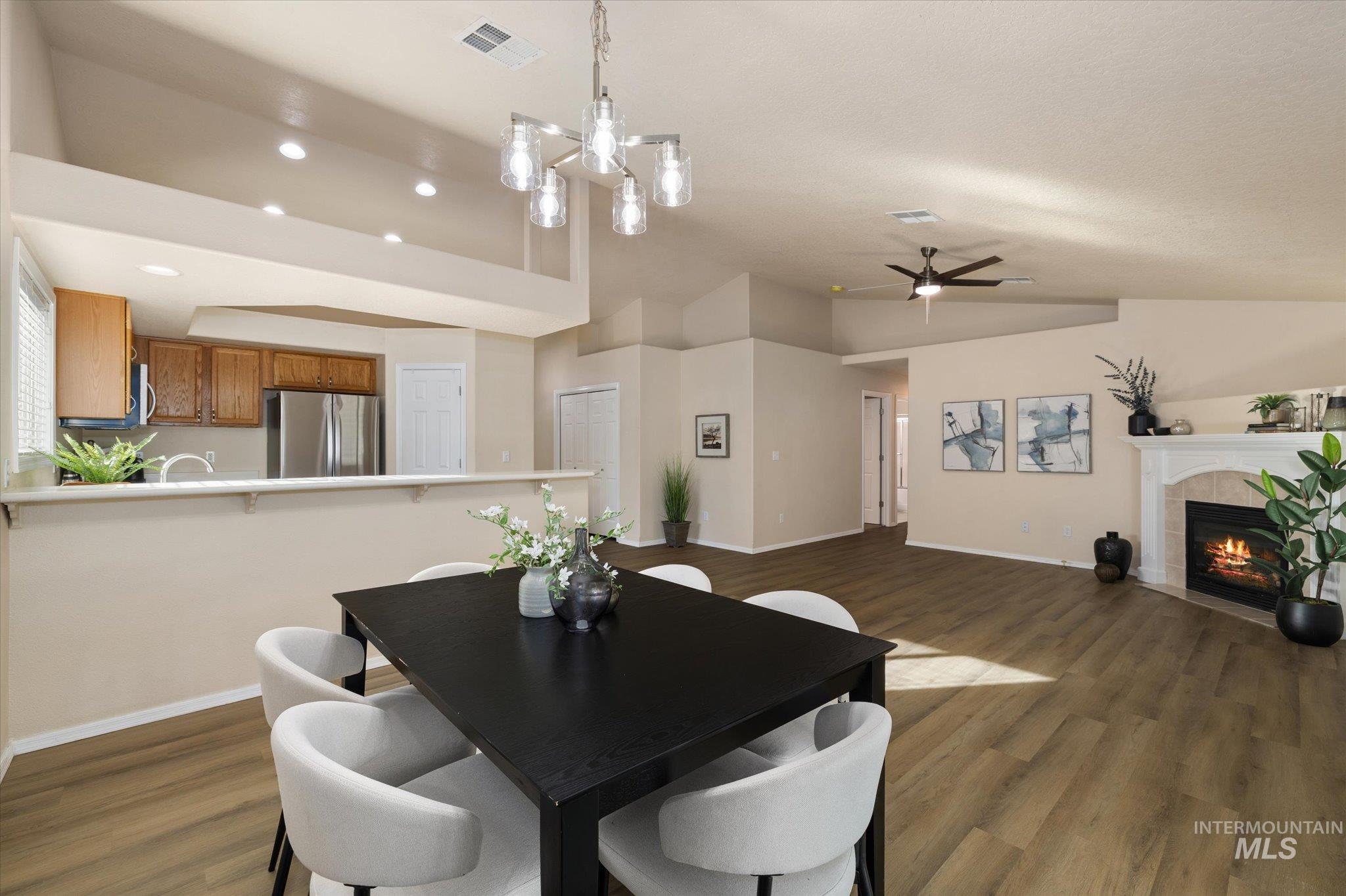 Dining room featuring lofted ceiling, dark wood-style flooring, a tiled fireplace, a chandelier, and a ceiling fan