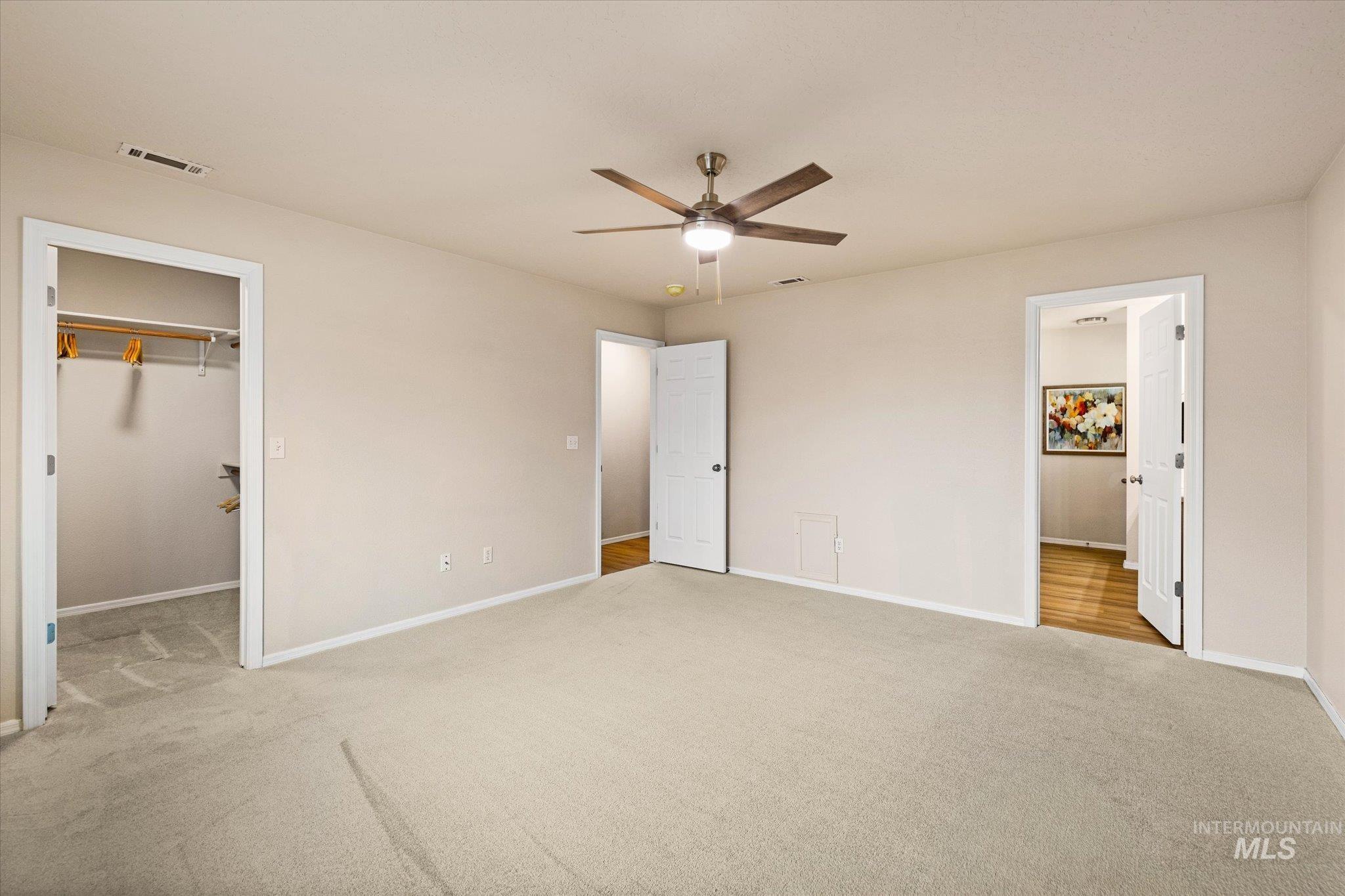 Unfurnished bedroom with light carpet, a walk in closet, and a ceiling fan
