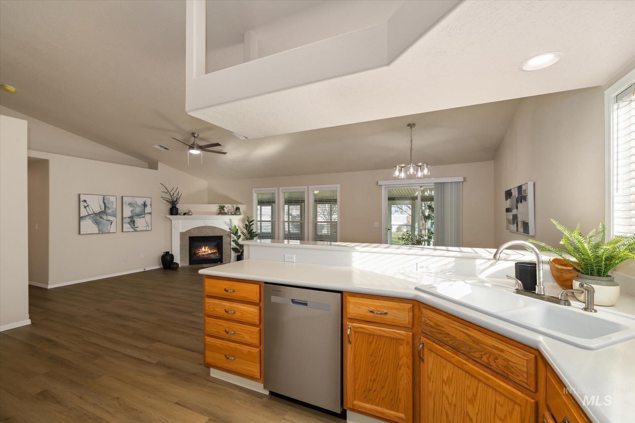 Kitchen featuring stainless steel dishwasher, a fireplace, lofted ceiling, light countertops, and dark wood finished floors