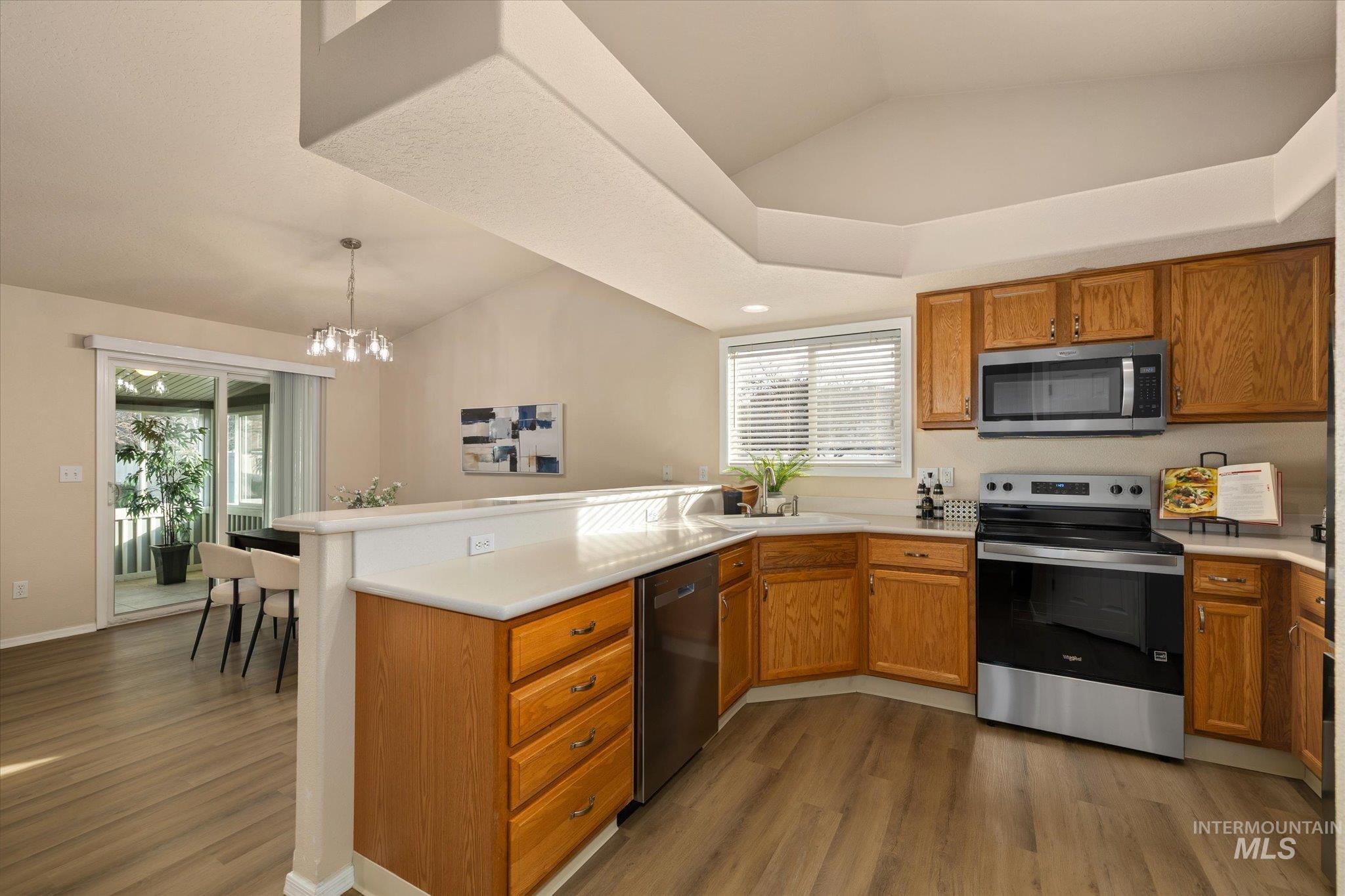Kitchen featuring appliances with stainless steel finishes, a peninsula, brown cabinetry, lofted ceiling, and light countertops