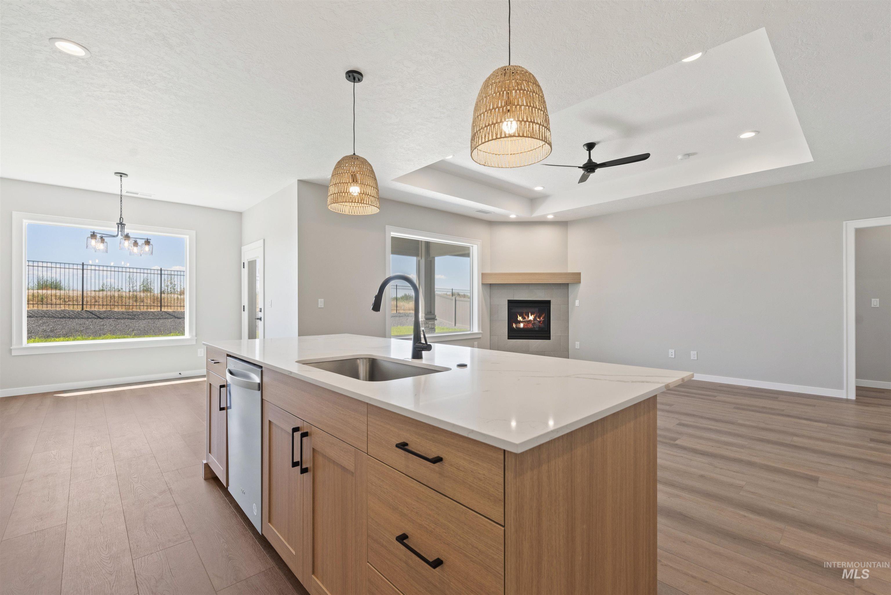 Kitchen featuring wood finished floors, open floor plan, a raised ceiling, a tiled fireplace, and recessed lighting