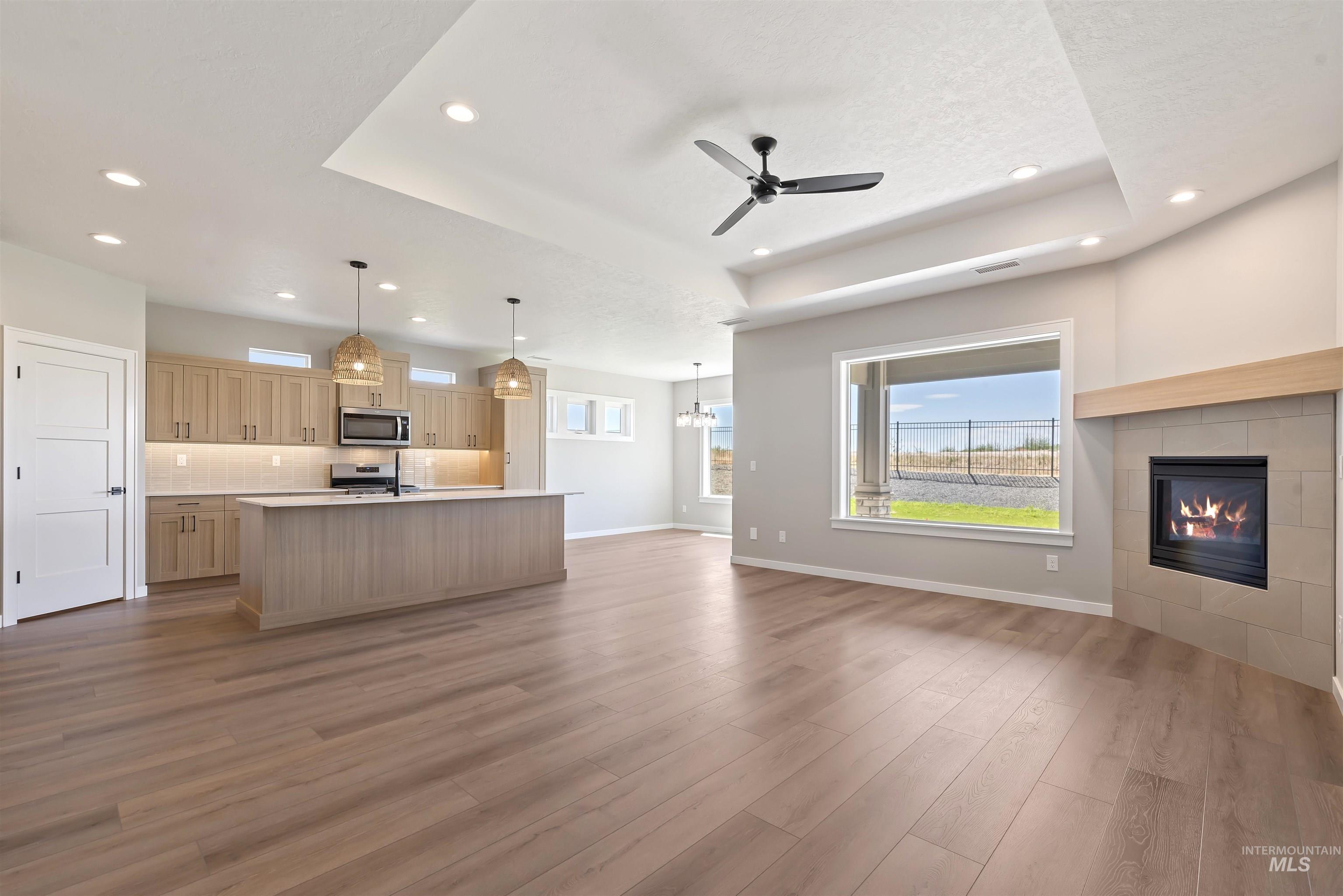 Unfurnished living room with a raised ceiling, wood finished floors, ceiling fan, recessed lighting, and a textured ceiling