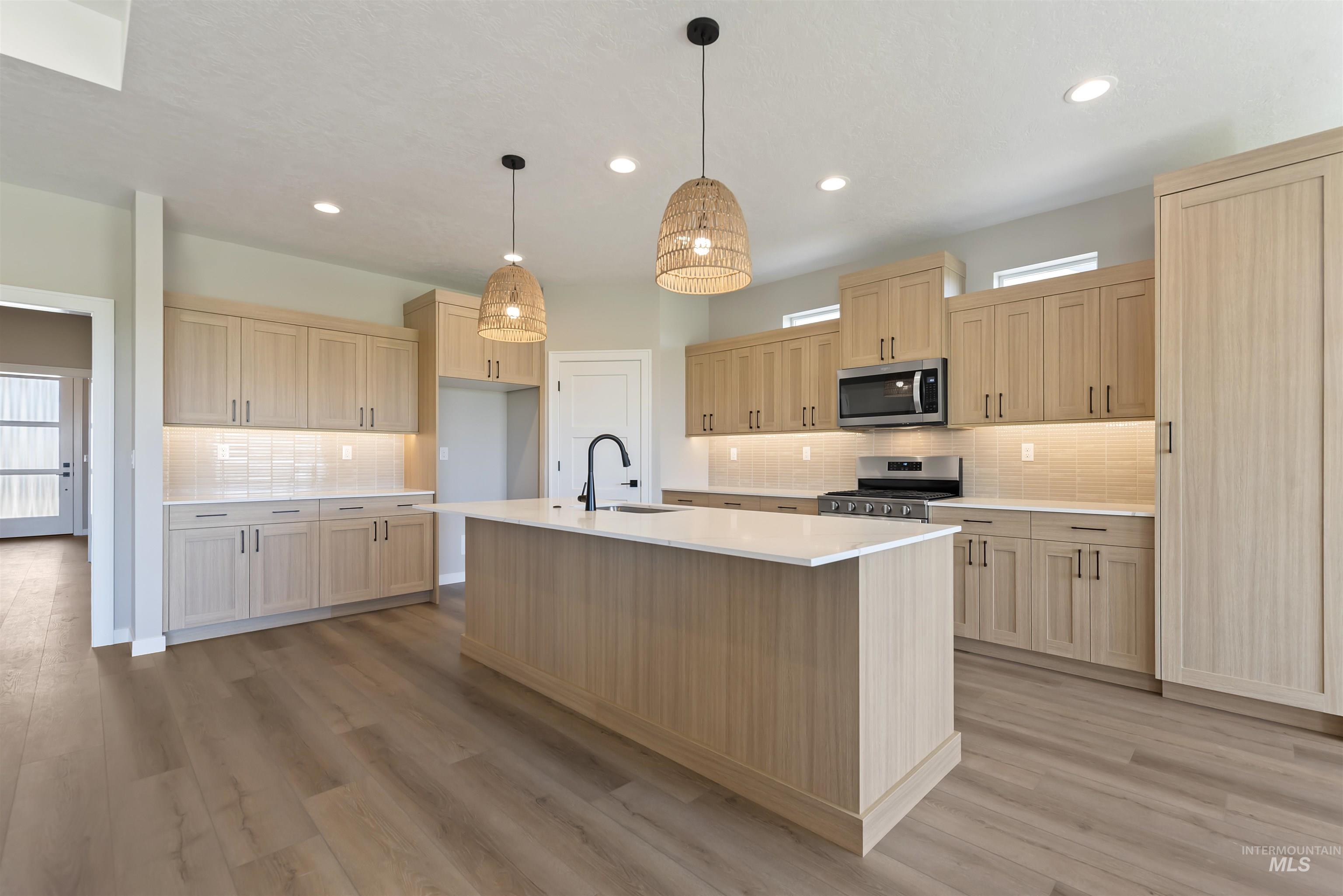 Kitchen featuring backsplash, stainless steel appliances, light brown cabinets, light countertops, and light wood-type flooring