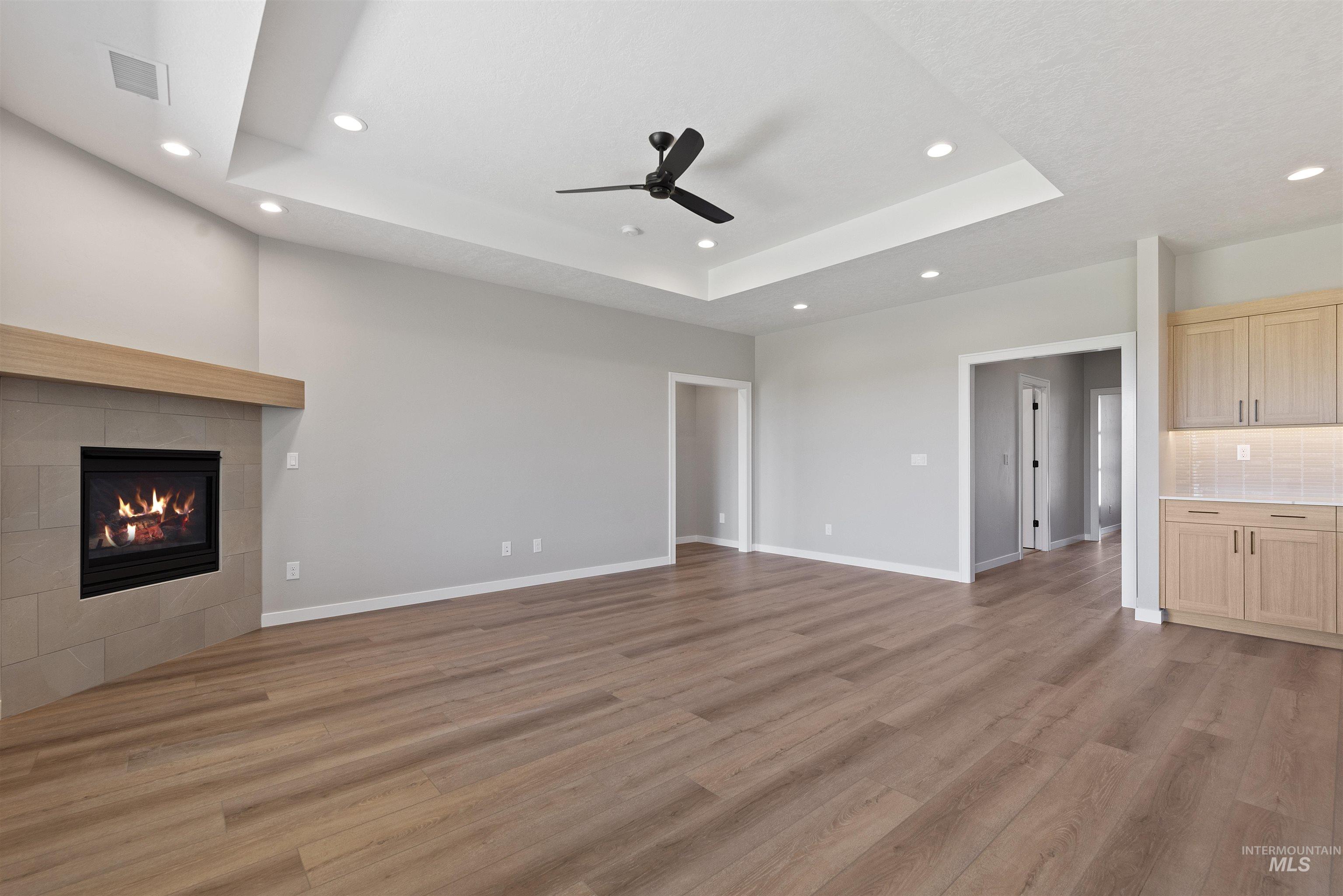 Unfurnished living room with recessed lighting, light wood-style floors, a raised ceiling, a tiled fireplace, and a ceiling fan