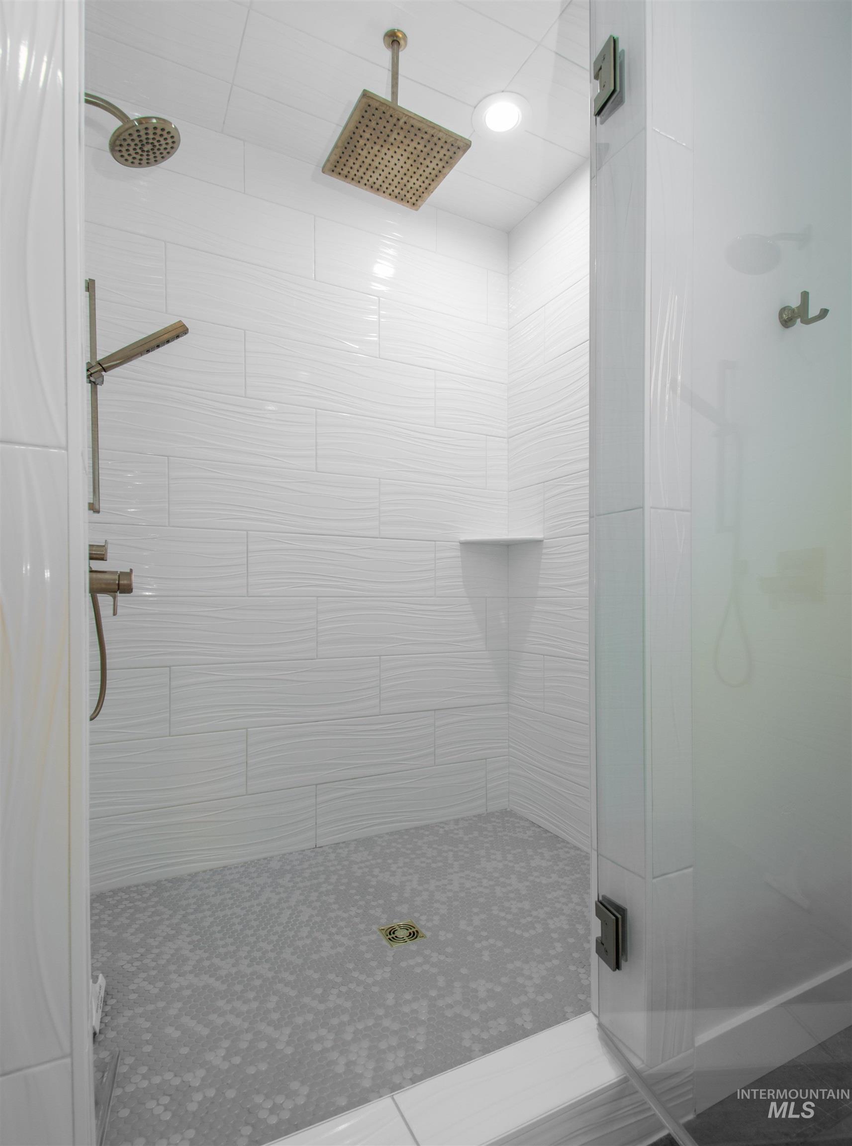 Walk-in shower featuring white wave-patterned wall tiles, a mosaic tile floor, and a built-in shower niche