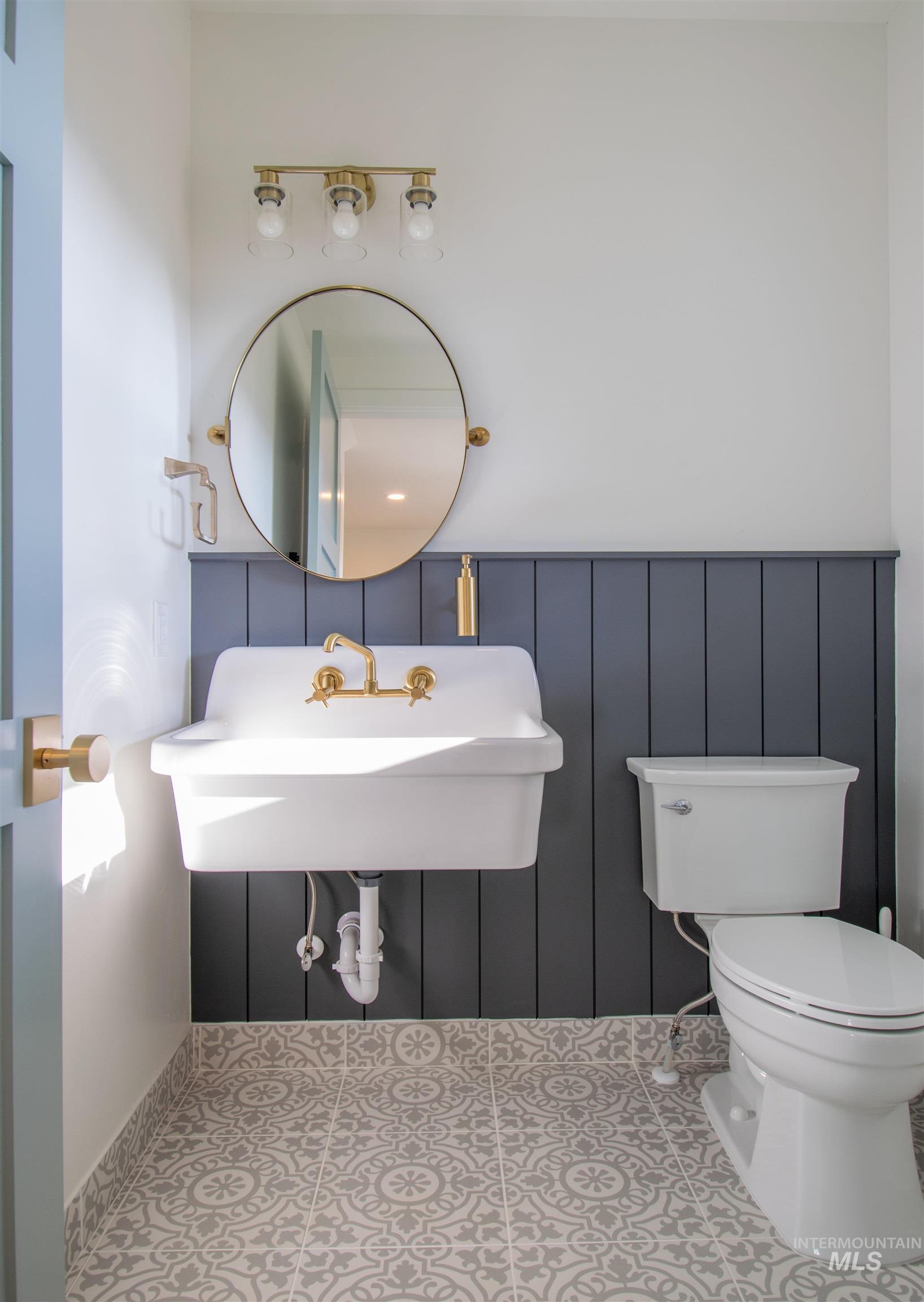 Bathroom featuring a wall-mounted sink with brass-finish faucet, a round mirror, and a three-light vanity fixture