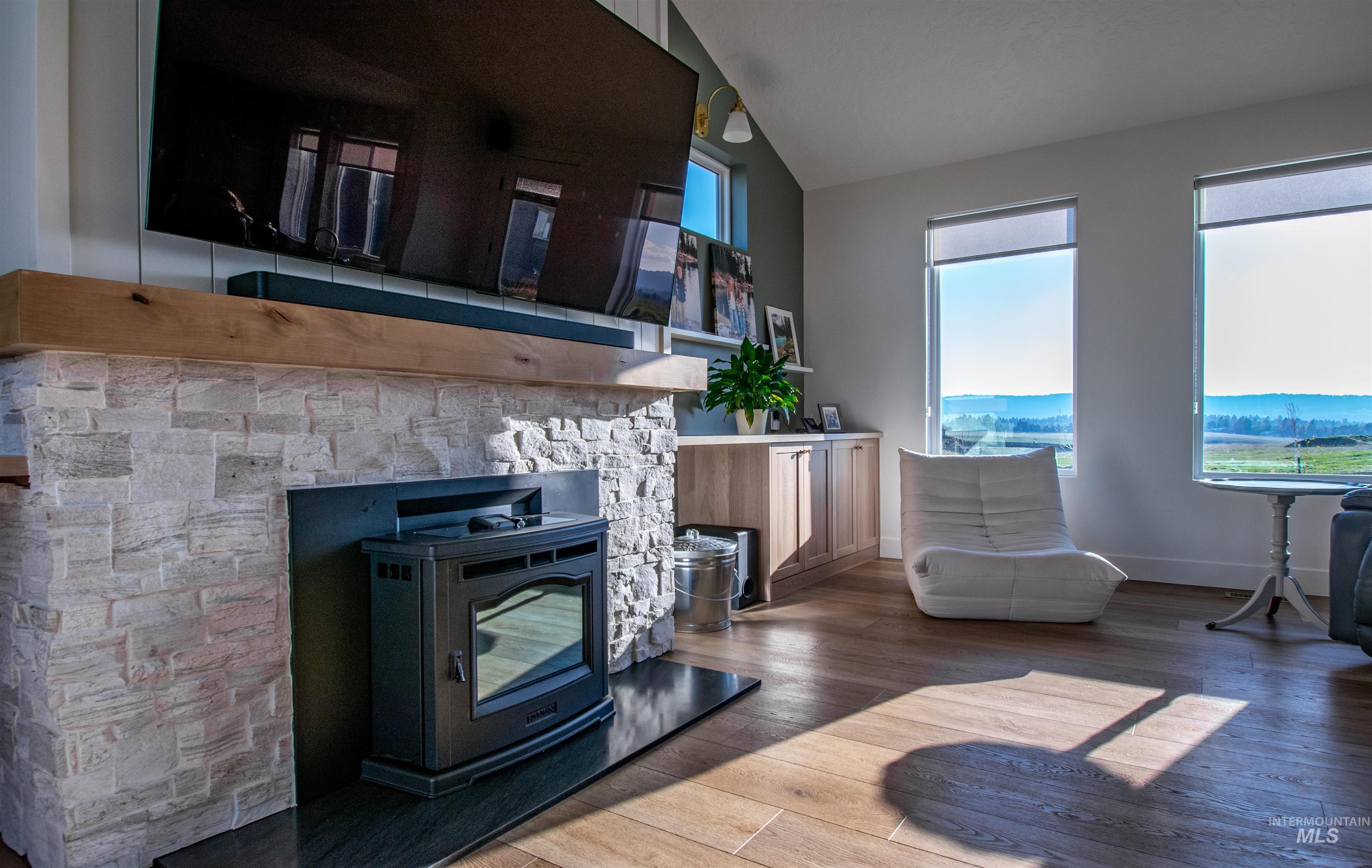 Light-filled interior featuring wood-finish flooring, a stacked stone fireplace with a substantial wood mantel, a built-in media center, and expansive windows
