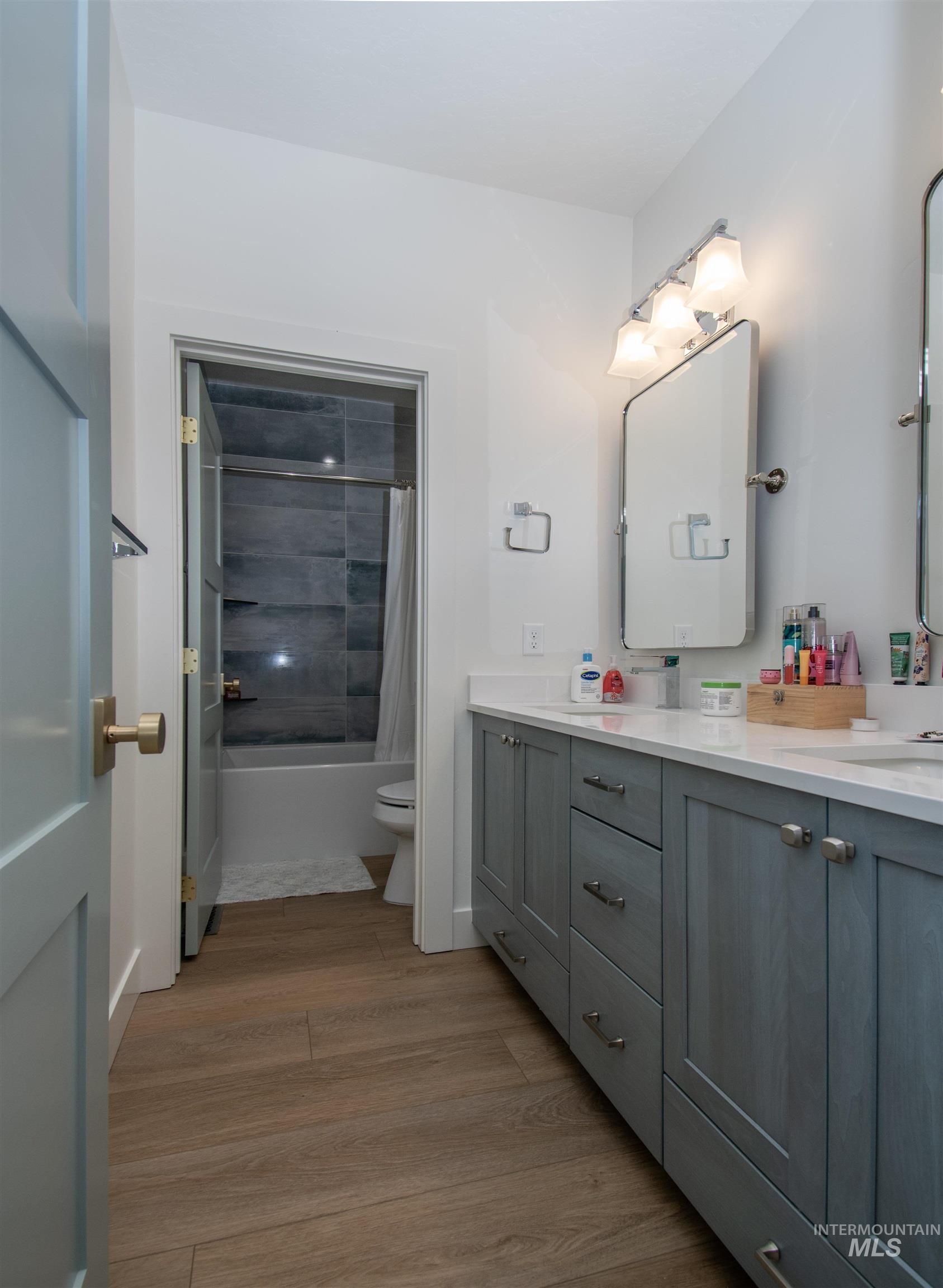 Bathroom featuring a double vanity with light gray cabinetry, white countertops, and wood-finish flooring