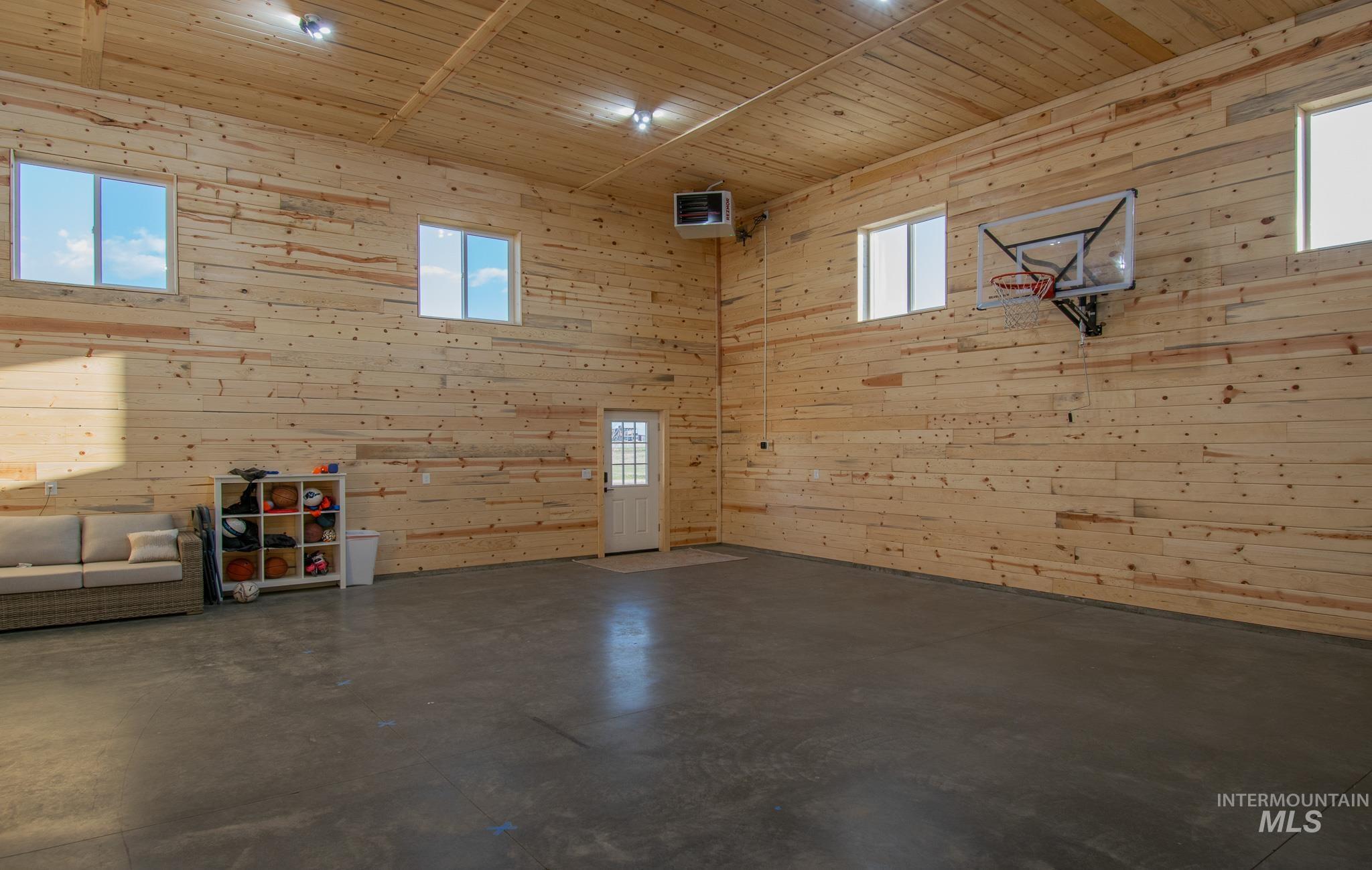 Spacious interior featuring natural wood plank walls and ceiling, high ceilings, four windows, a white entry door with glass panels, and a polished concrete floor