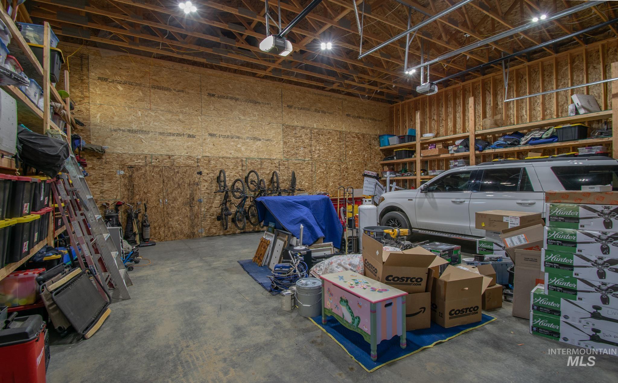 Spacious garage featuring exposed wood framing, high ceilings with visible rafters, and overhead lighting
