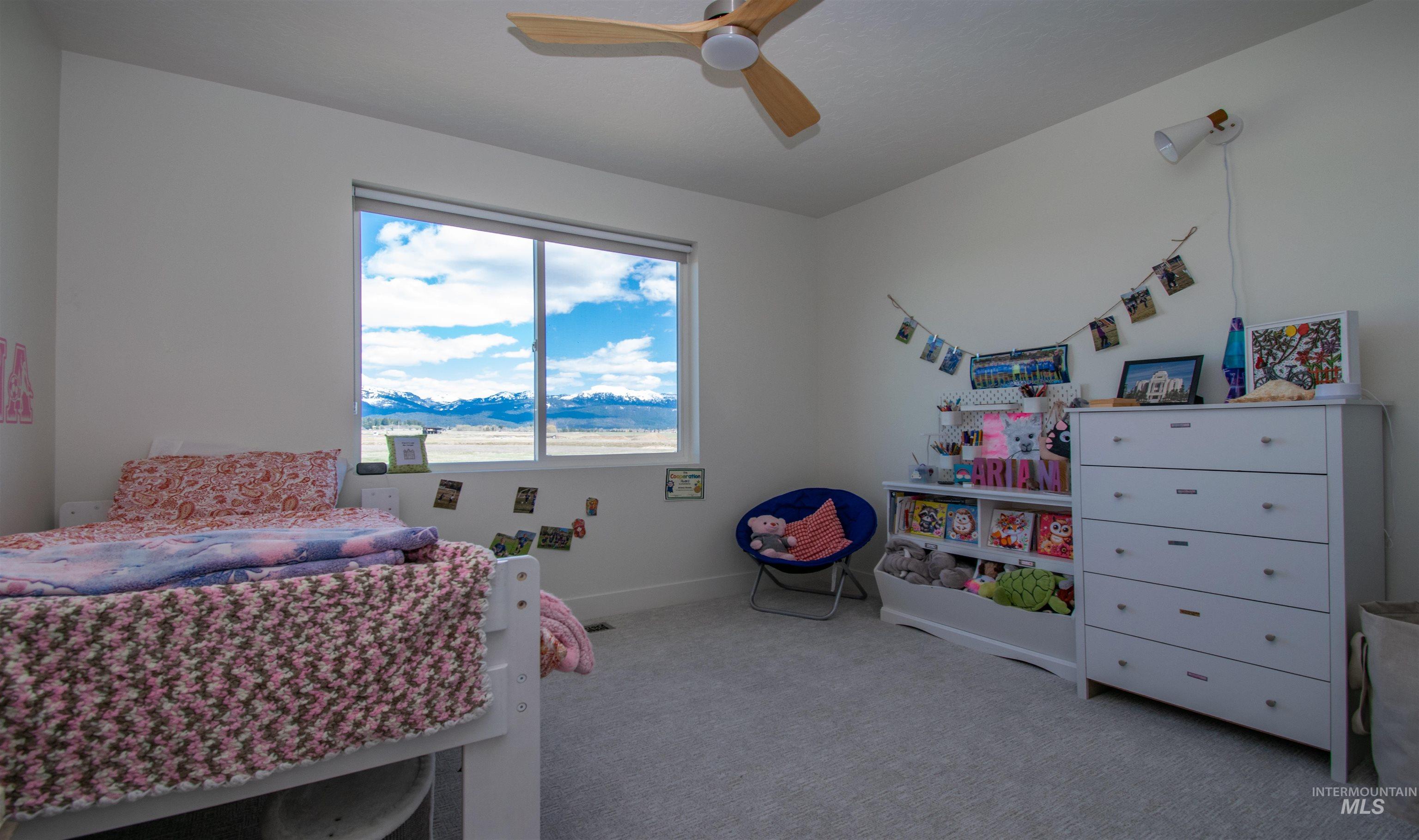 Room featuring a large window, light gray carpeting, neutral wall finishes, a ceiling fan, and a wall-mounted light fixture