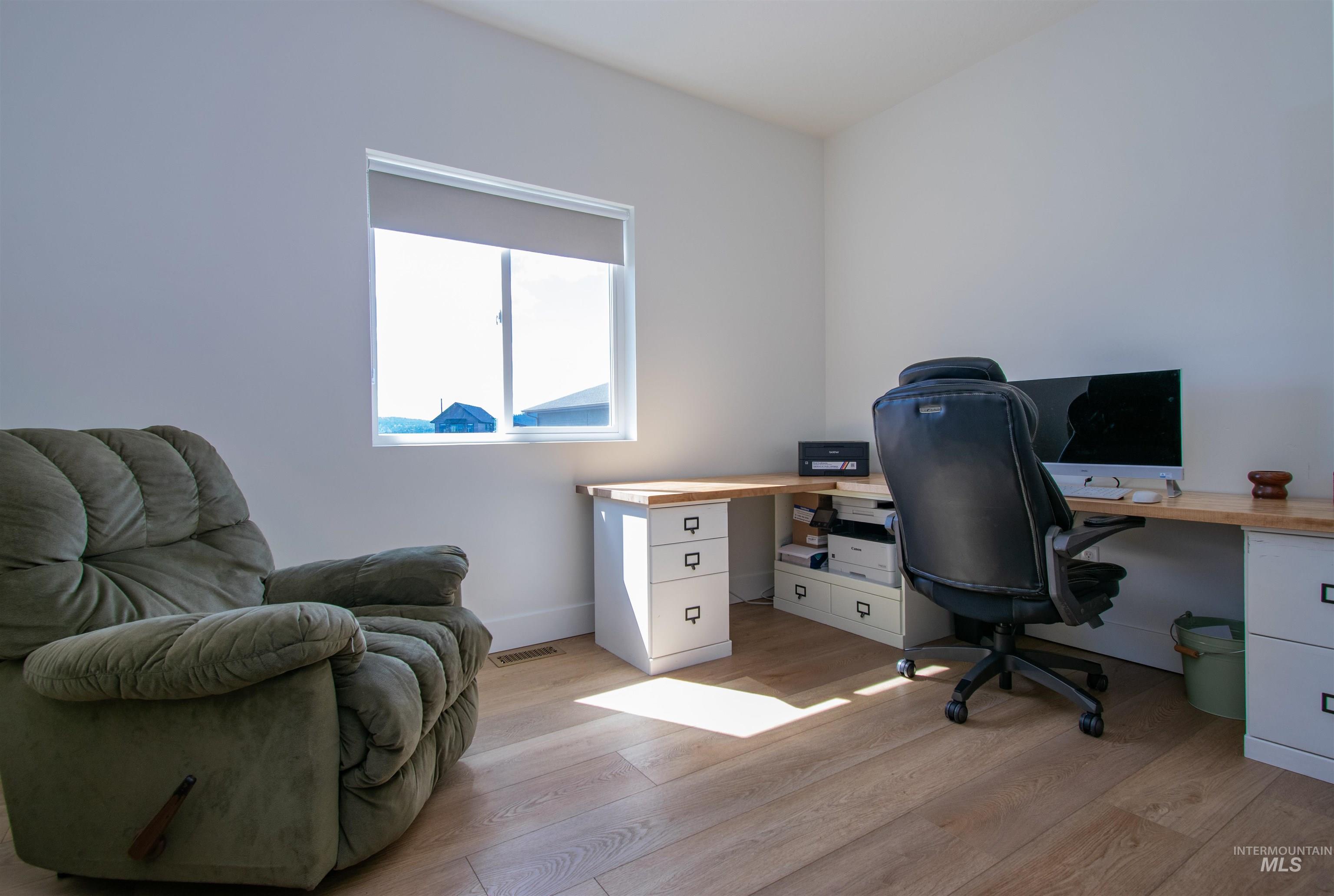 Bright room featuring a window with a roller shade, wood-finish flooring, and white walls