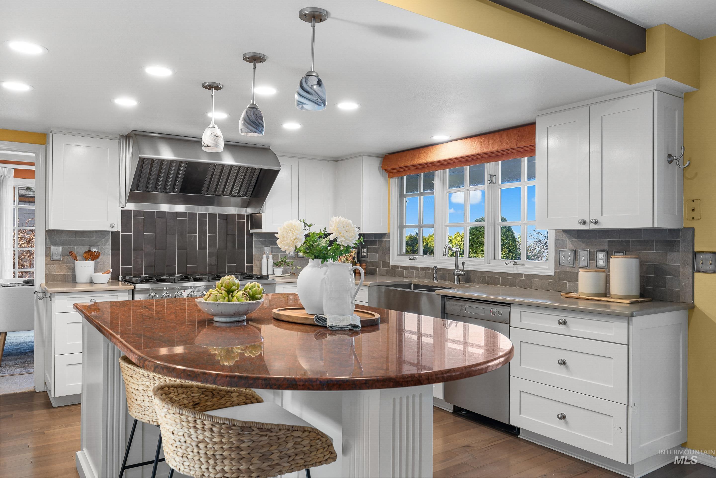 Kitchen with white cabinets, stainless steel appliances, a kitchen breakfast bar, dark stone counters, and dark wood finished floors