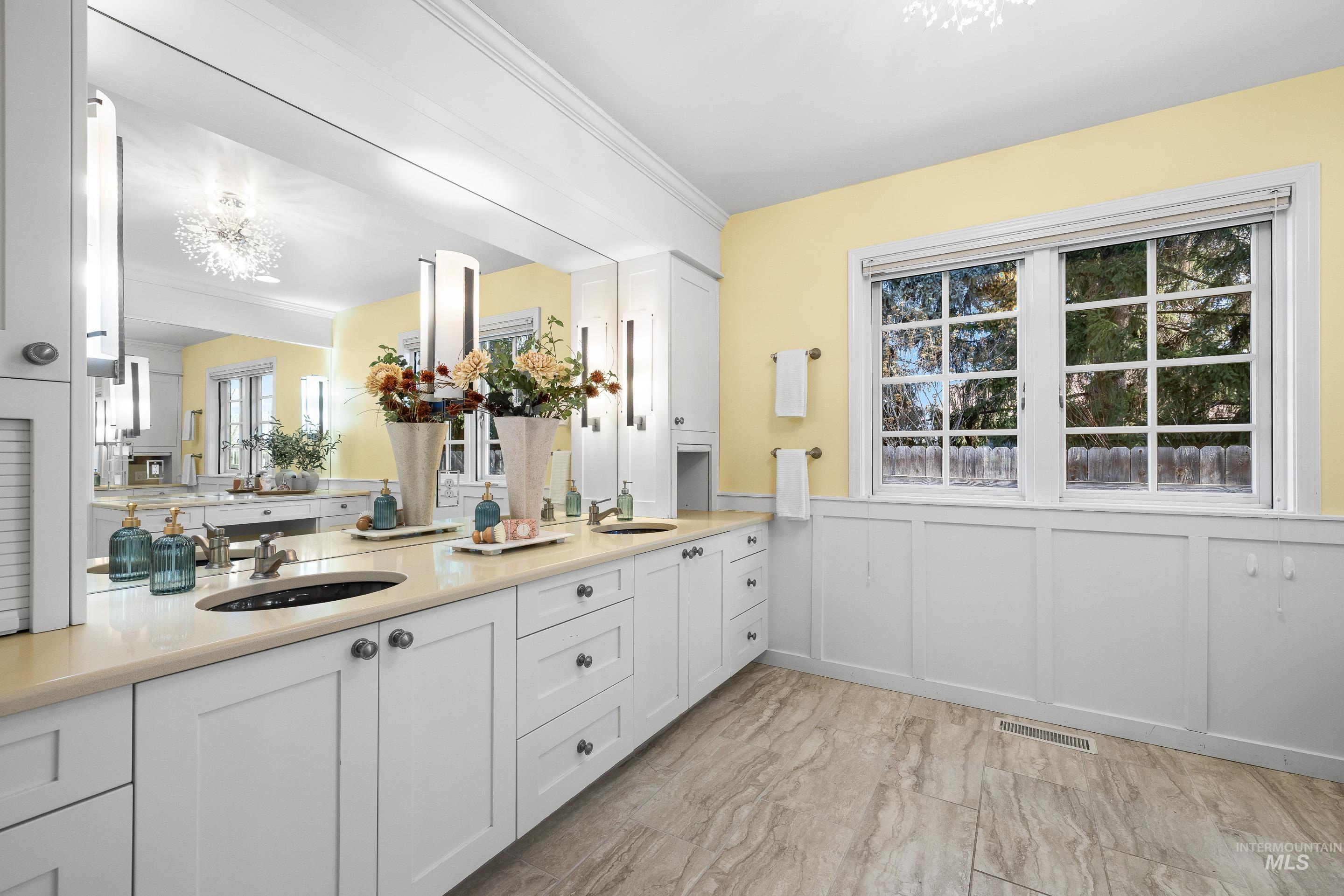 Bathroom with a decorative wall, wainscoting, double vanity, ornamental molding, and a chandelier