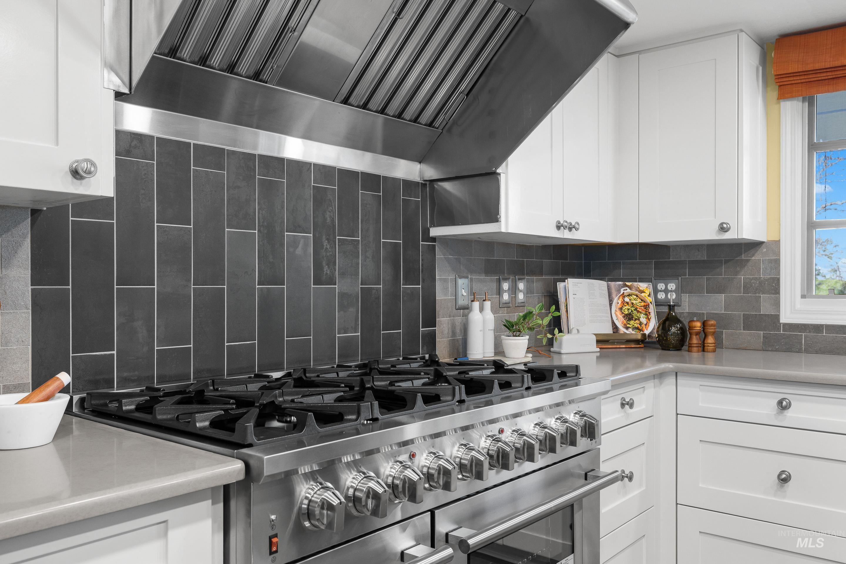 Kitchen with extractor fan, white cabinetry, double oven range, decorative backsplash, and light stone countertops