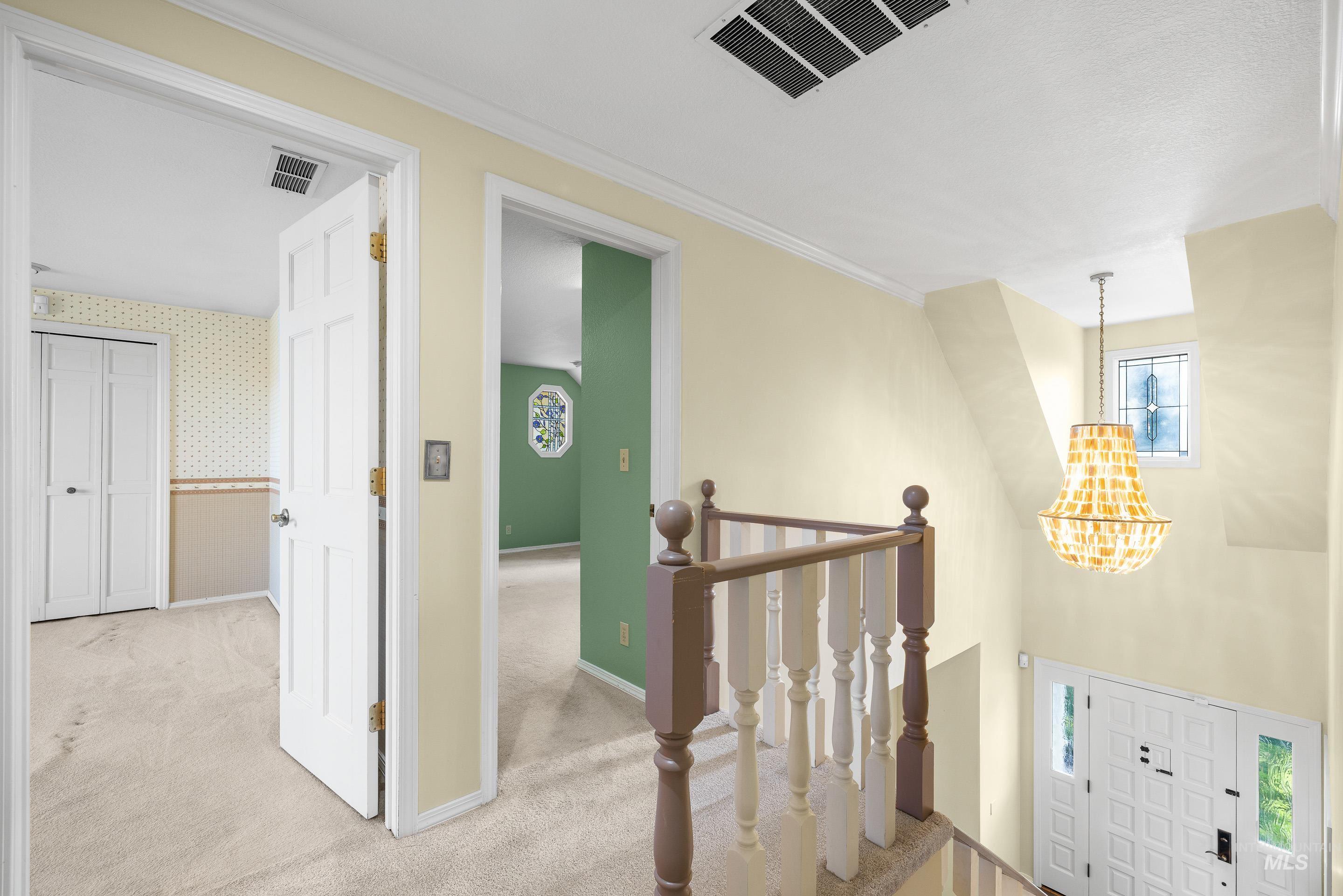 Hallway with light colored carpet, suspended lighting, healthy amount of natural light, wallpapered walls, and ornamental molding
