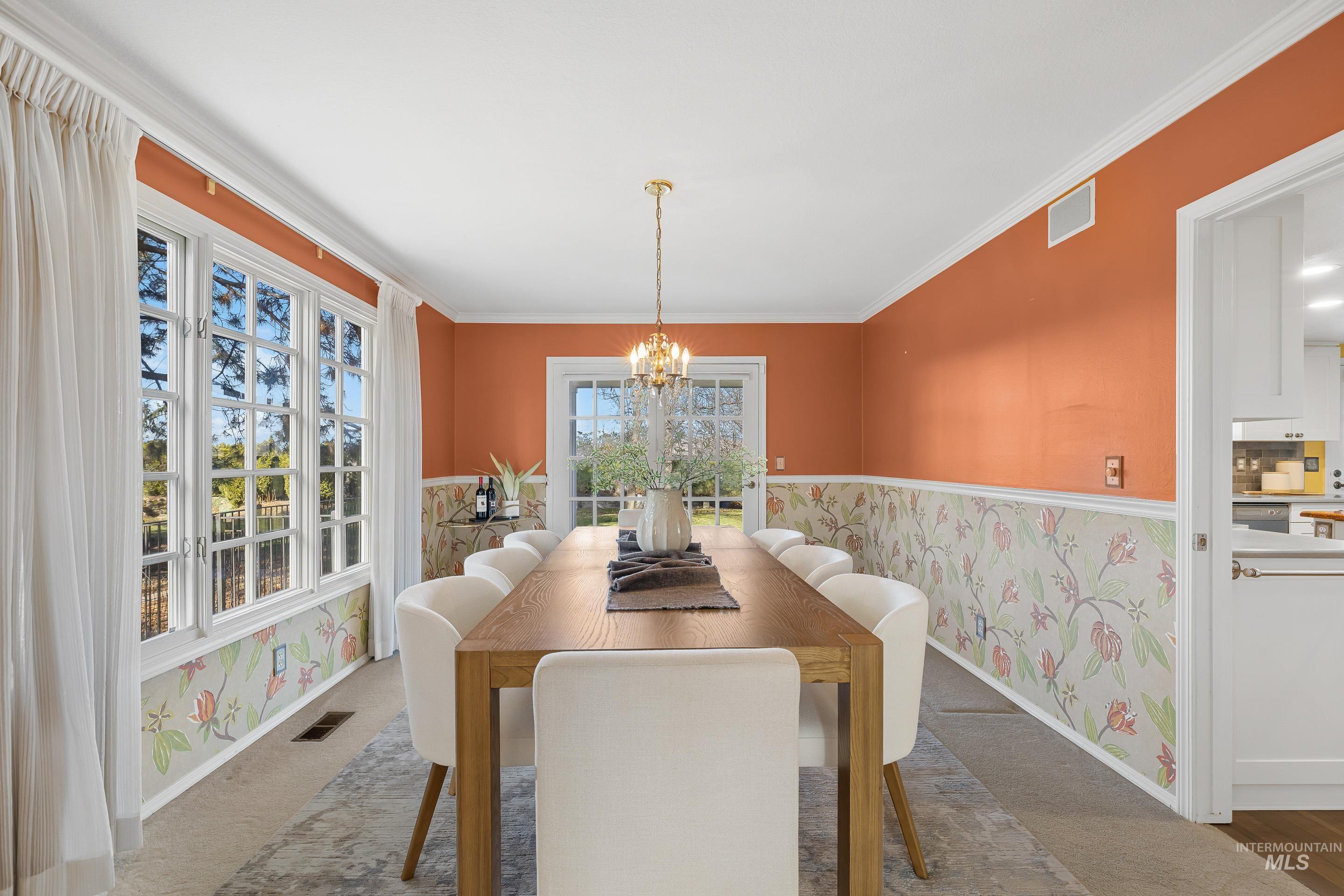 Carpeted dining area featuring wallpapered walls, suspended lighting, crown molding, and a wainscoted wall