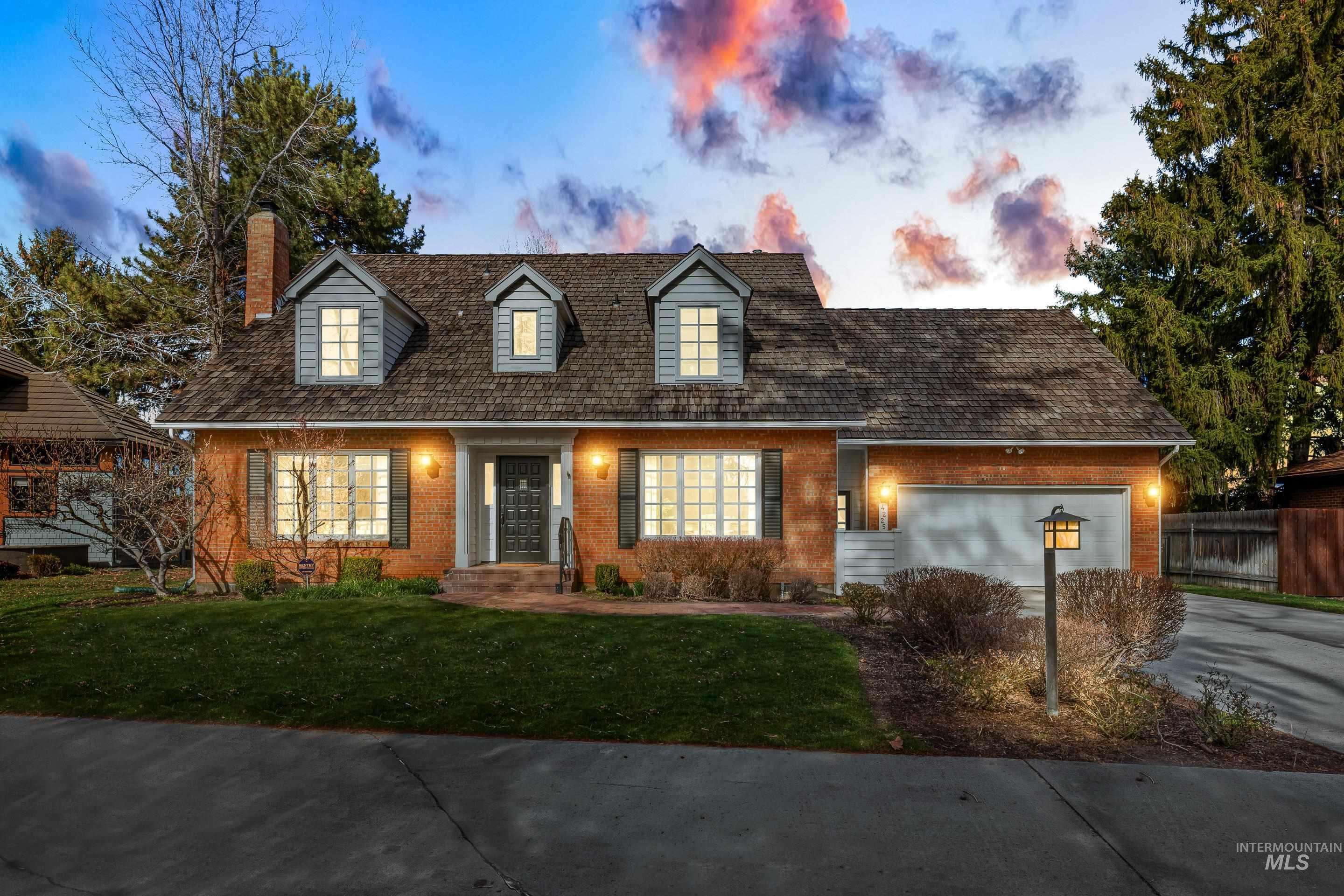 Cape cod-style house with a garage, a front lawn, brick siding, driveway, and a chimney