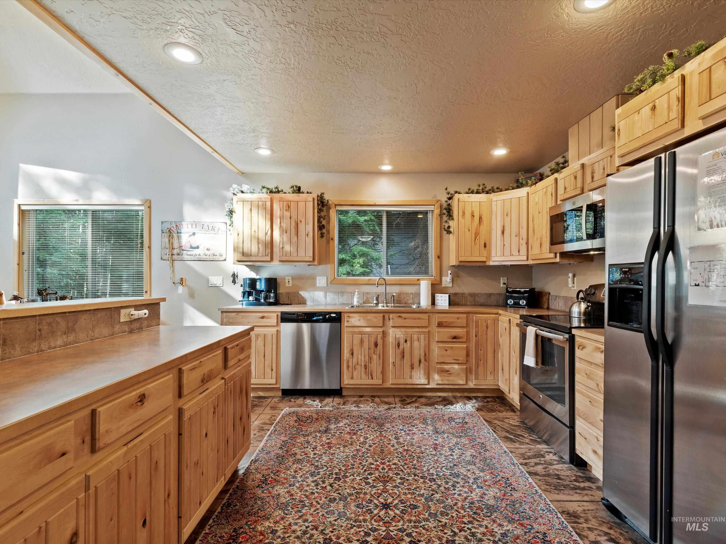 Kitchen featuring appliances with stainless steel finishes, a textured ceiling, light countertops, light brown cabinets, and recessed lighting