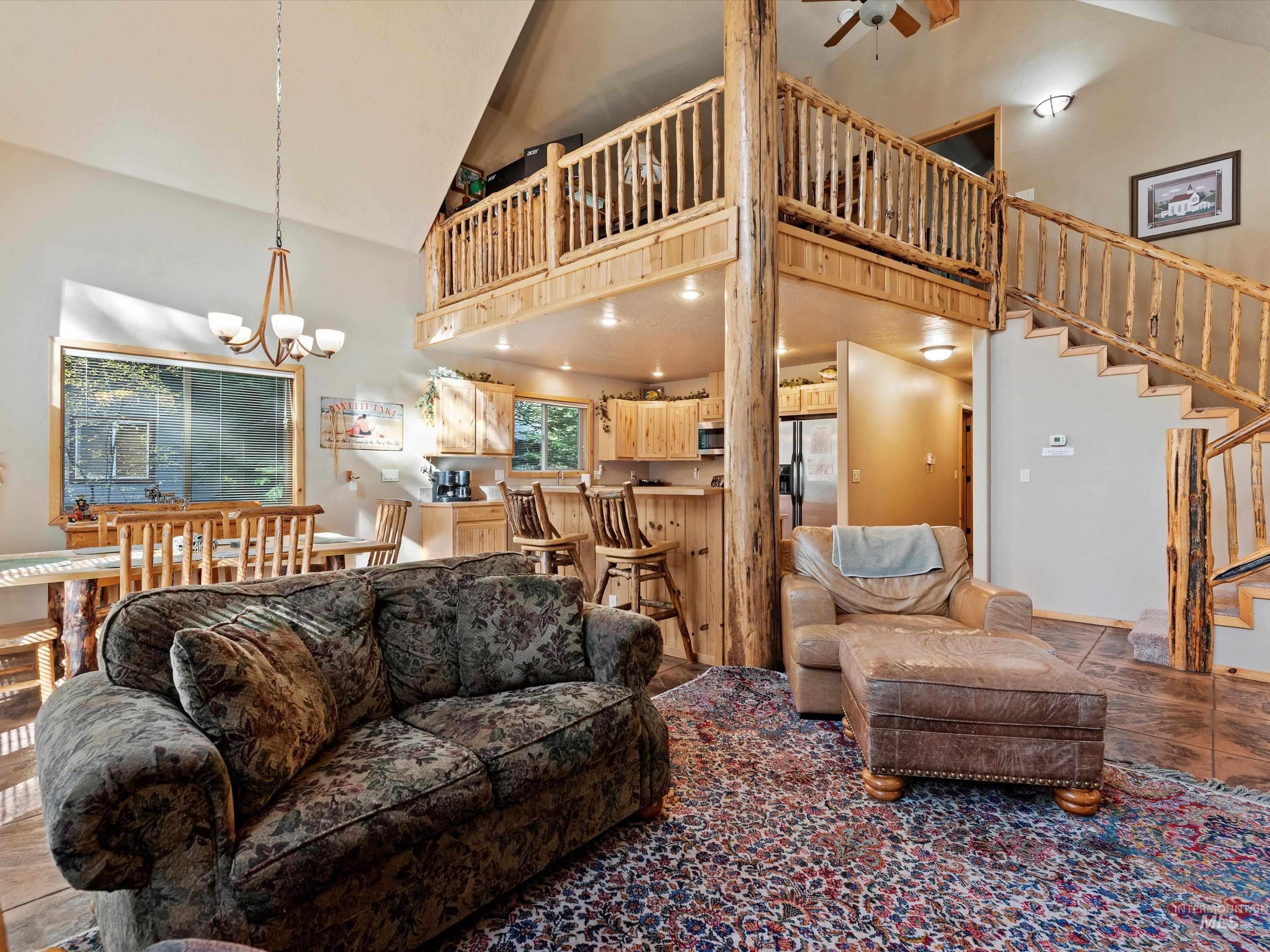 Living room featuring high vaulted ceiling, stairway, a chandelier, and a ceiling fan