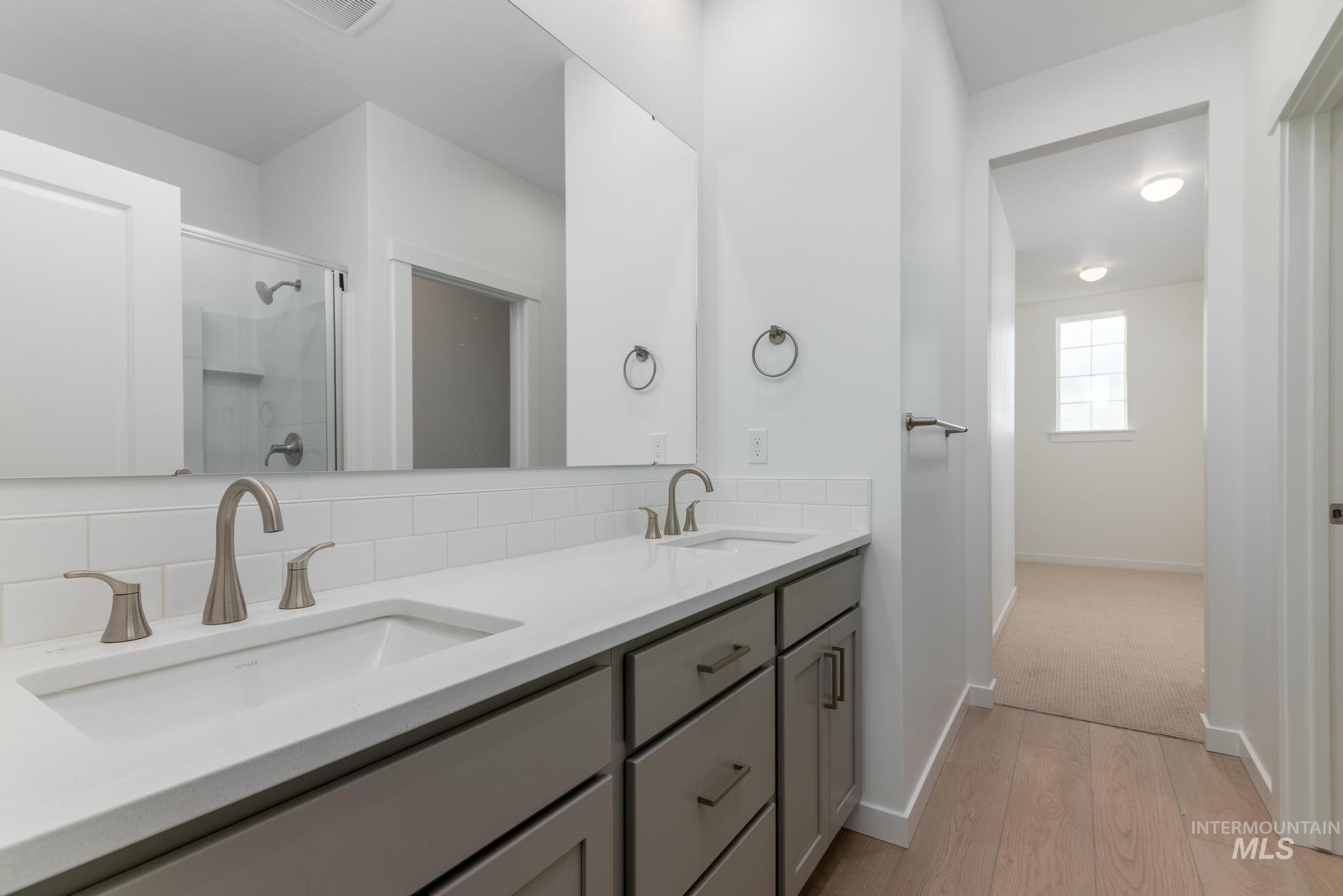 Full bathroom with light wood-type flooring, a shower stall, double vanity, and decorative backsplash