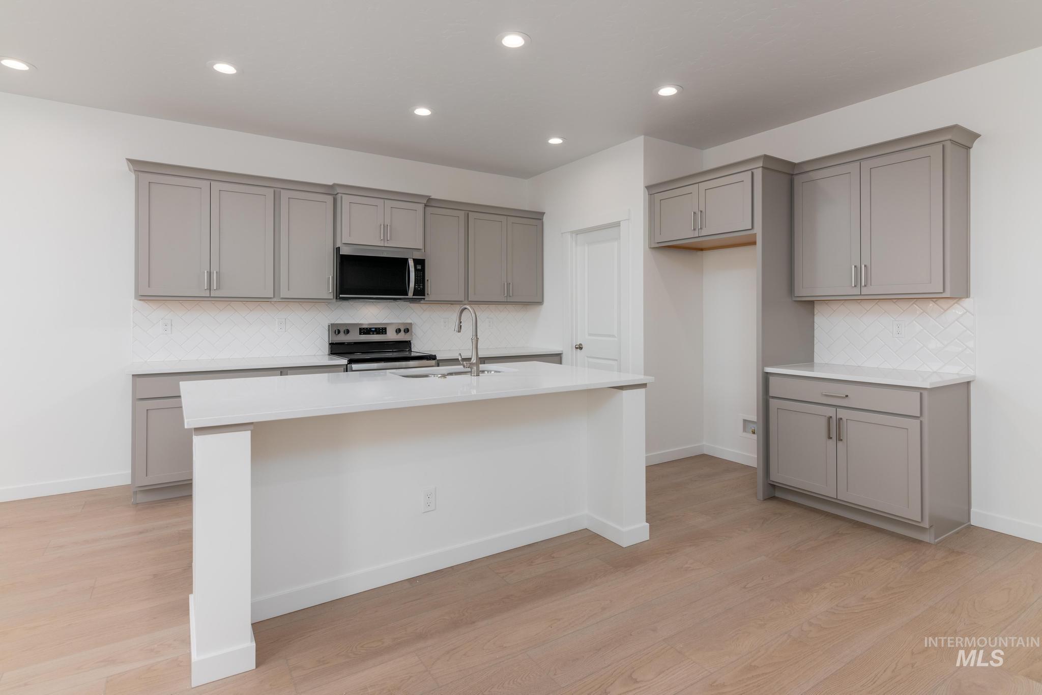 Kitchen with gray cabinets, backsplash, and recessed lighting
