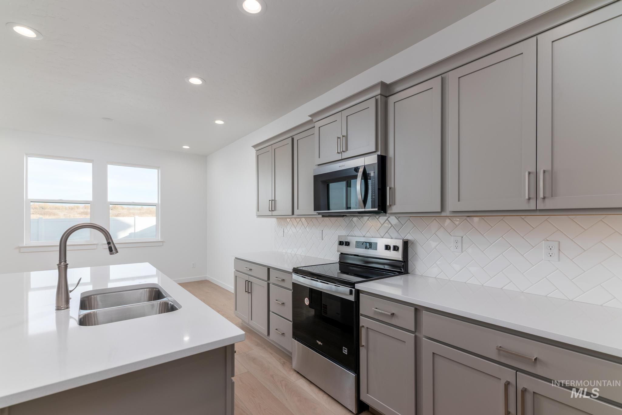 Kitchen featuring gray cabinets, stainless steel appliances, recessed lighting, light wood-type flooring, and tasteful backsplash
