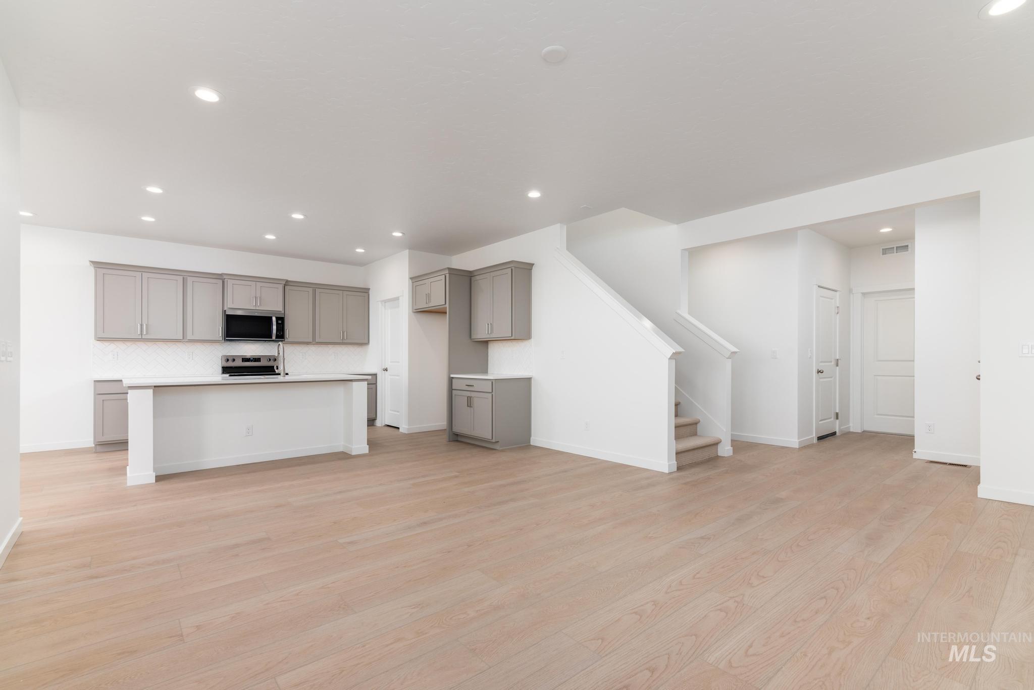 Kitchen with gray cabinetry, a center island with sink, light countertops, recessed lighting, and light wood finished floors